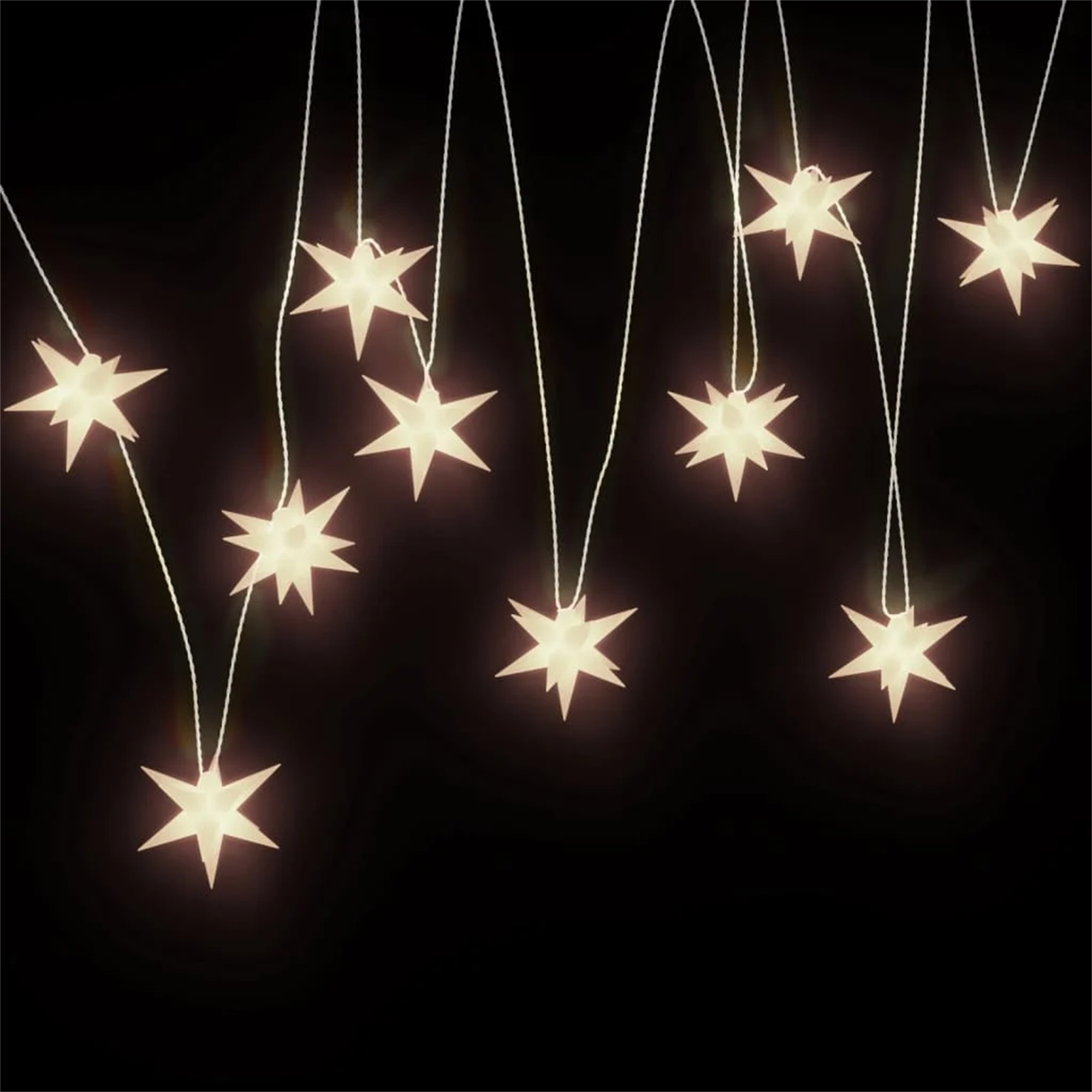 Eine Nachtszene zeigt sternförmige Lichter, die vor schwarzem Hintergrund hängen.