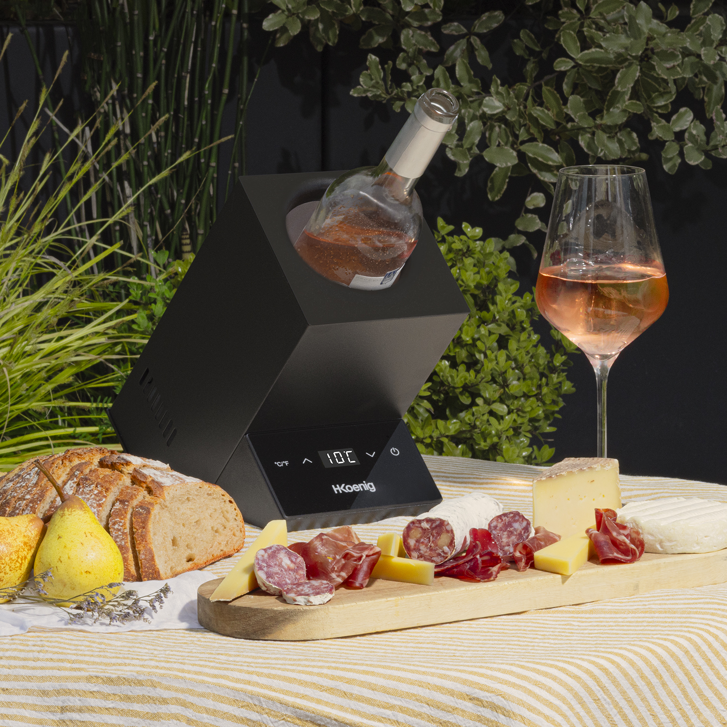 Un tavolo con vino, cibo e un refrigeratore per vino. Include pane, formaggio, salame, pere e fiori.