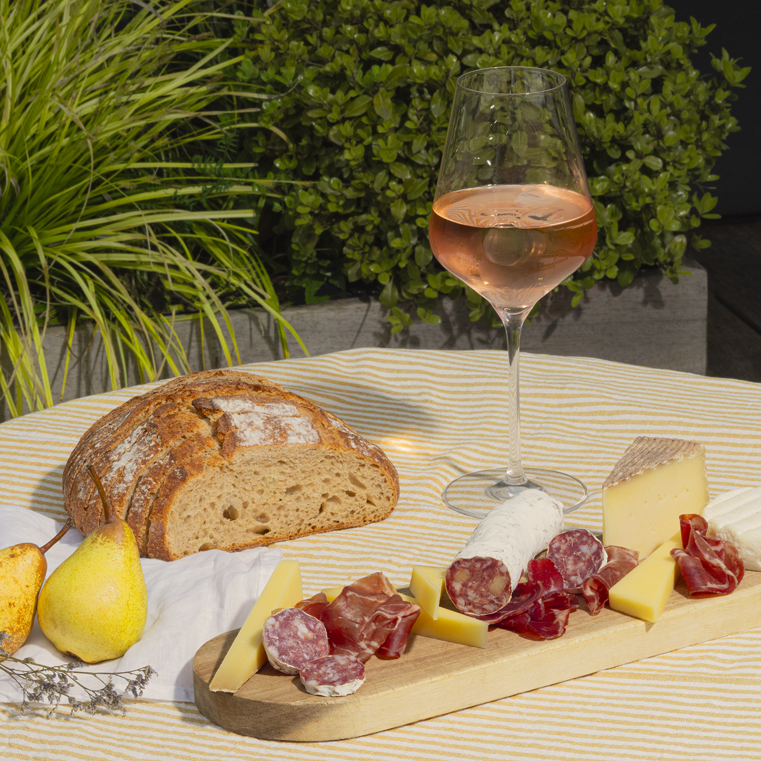 Un tavolo con pane, salumi, formaggio, pere e vino, all'aperto.