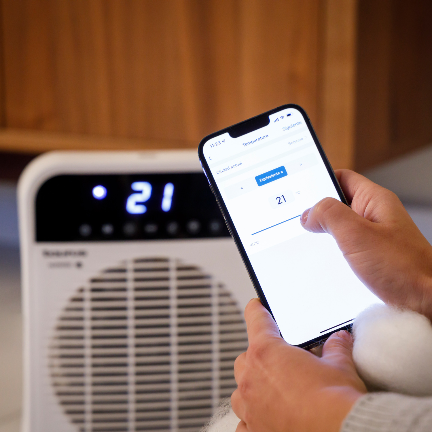 Osoba używa smartfona do sterowania białym grzejnikiem. Ekran pokazuje temperaturę.