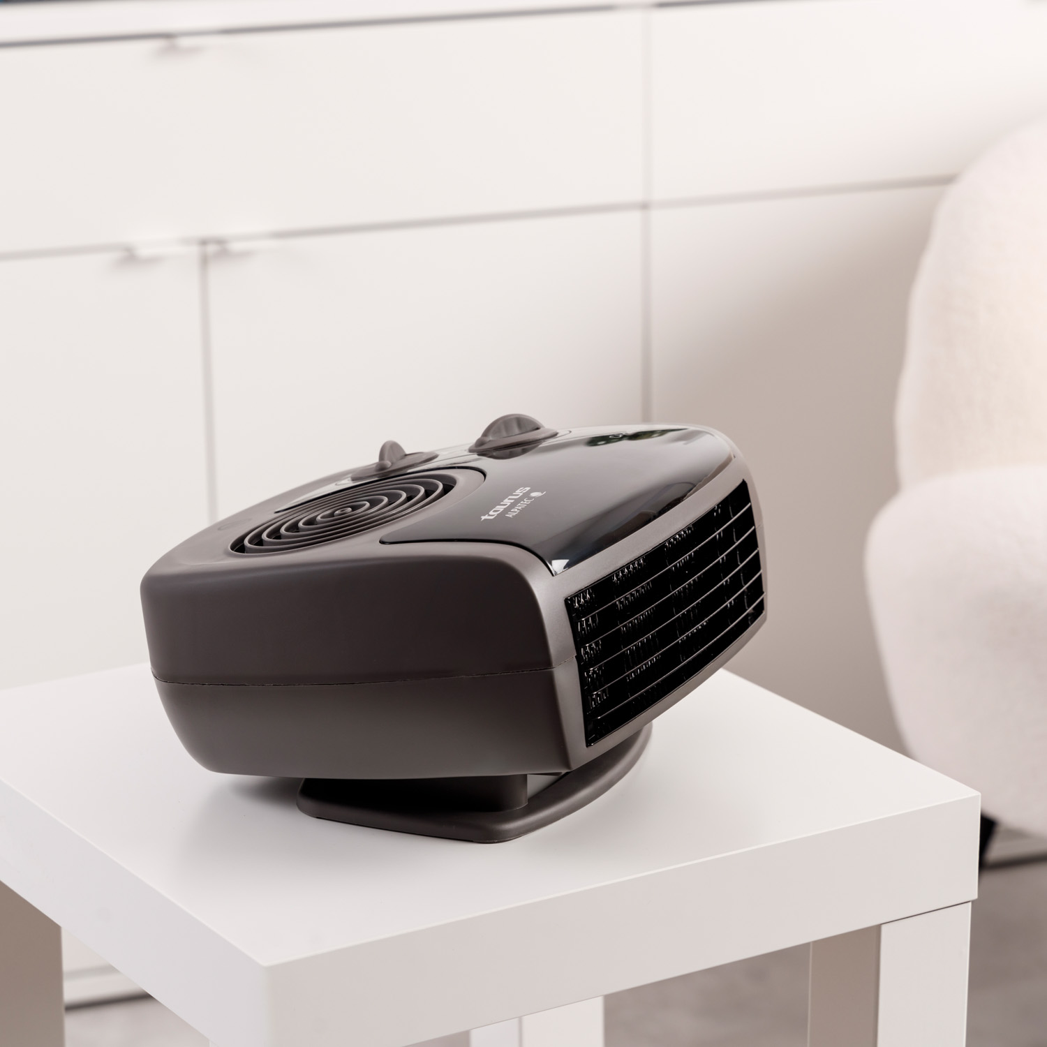 Czarny grzejnik na białym stole. Białe krzesło i szafka w tle.