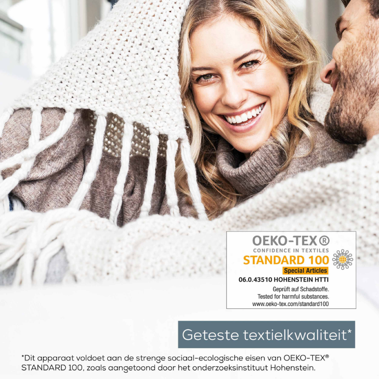 Donna sorride sotto coperta con uomo. Testo: Oeko-Tex Standard 100.