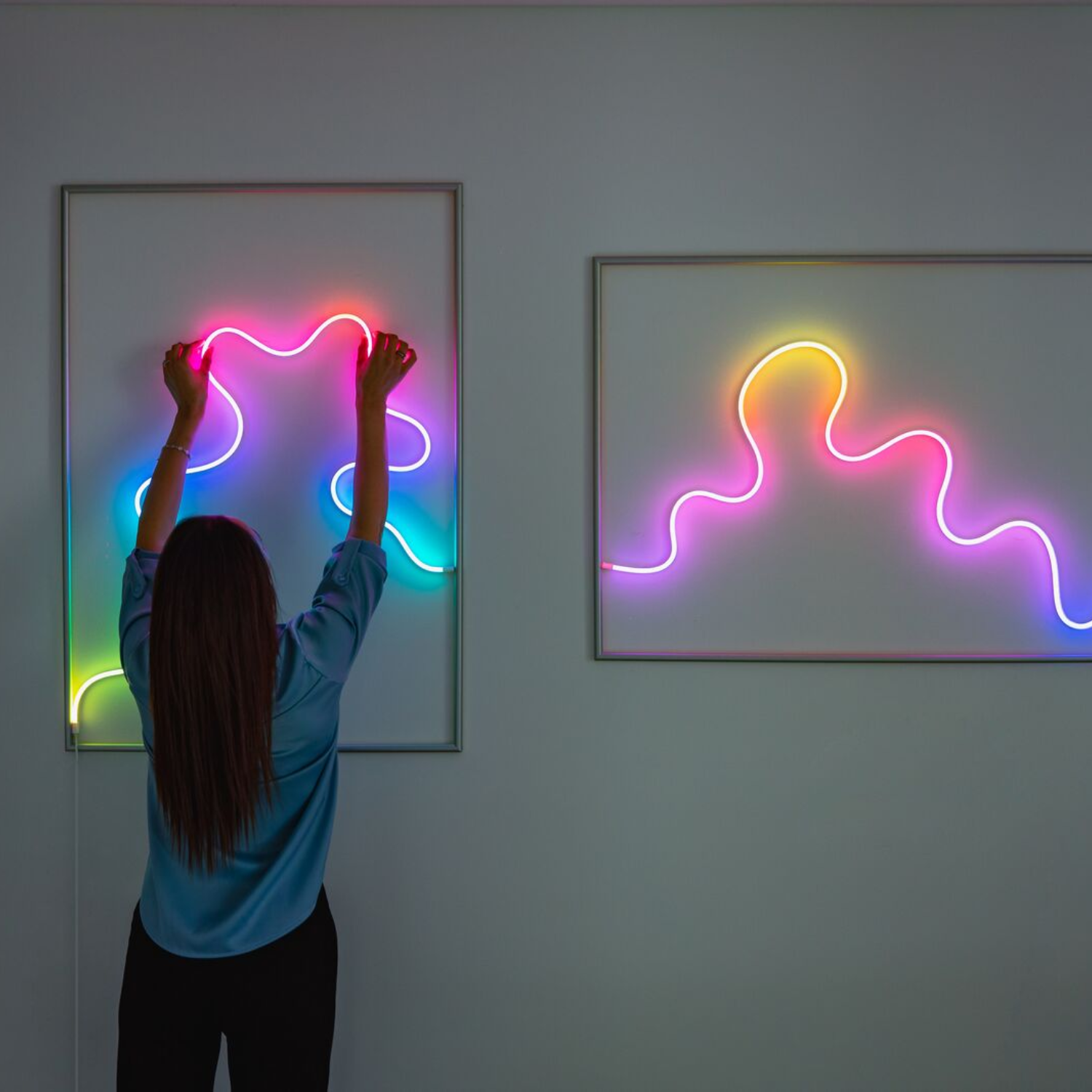 Osoba wieszająca neonowe dzieła sztuki na ścianie. Dwa oprawione dzieła sztuki ze światłami neonowymi.