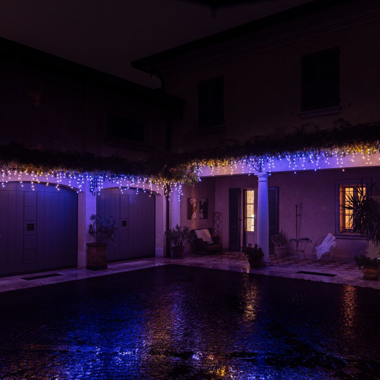 Hof bei Nacht mit Lichtern. Blaue Lichter auf dem Dach und weiße Lichter auf der Veranda.