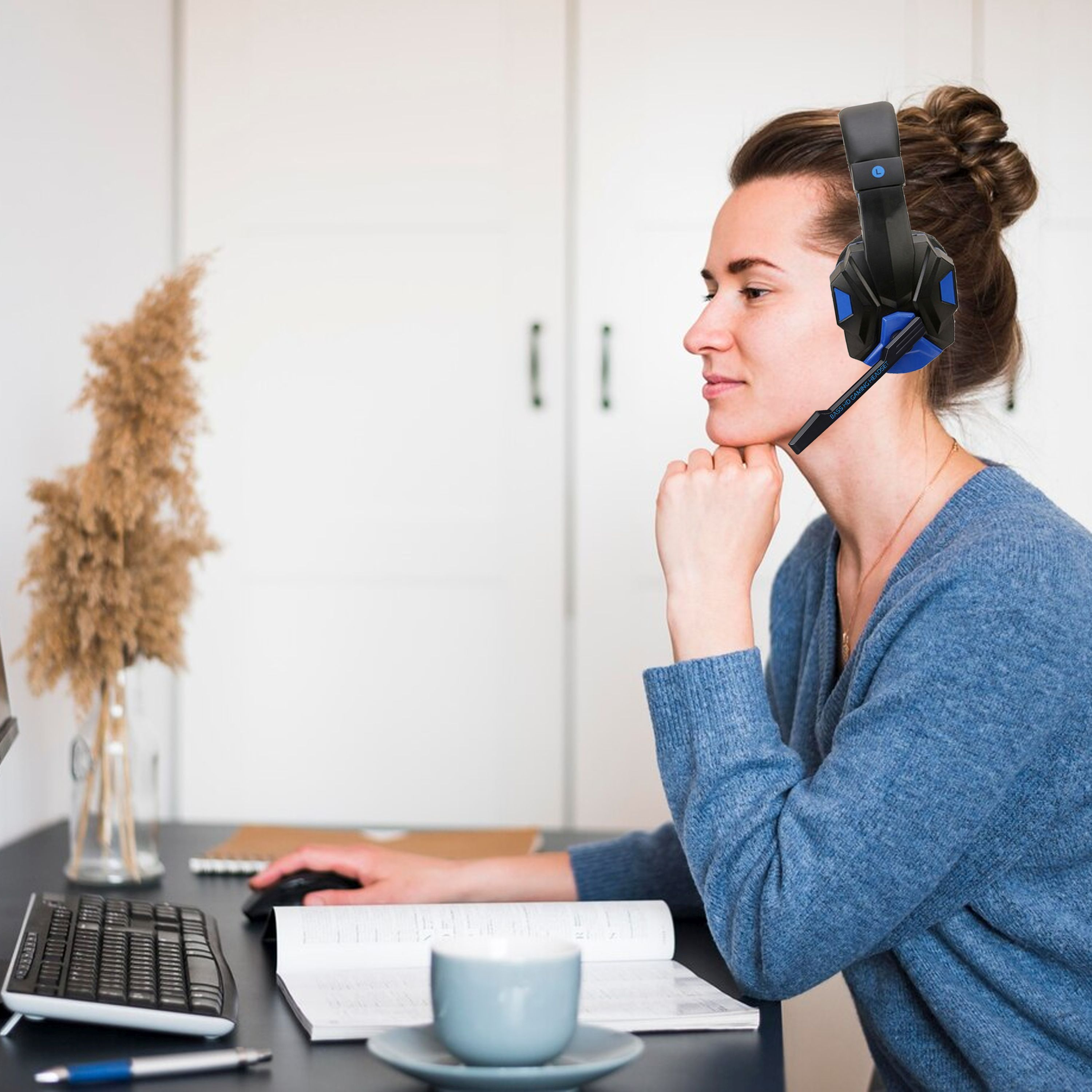 Donna con cuffie, guarda uno schermo del computer, con un libro e una tazza vicini.