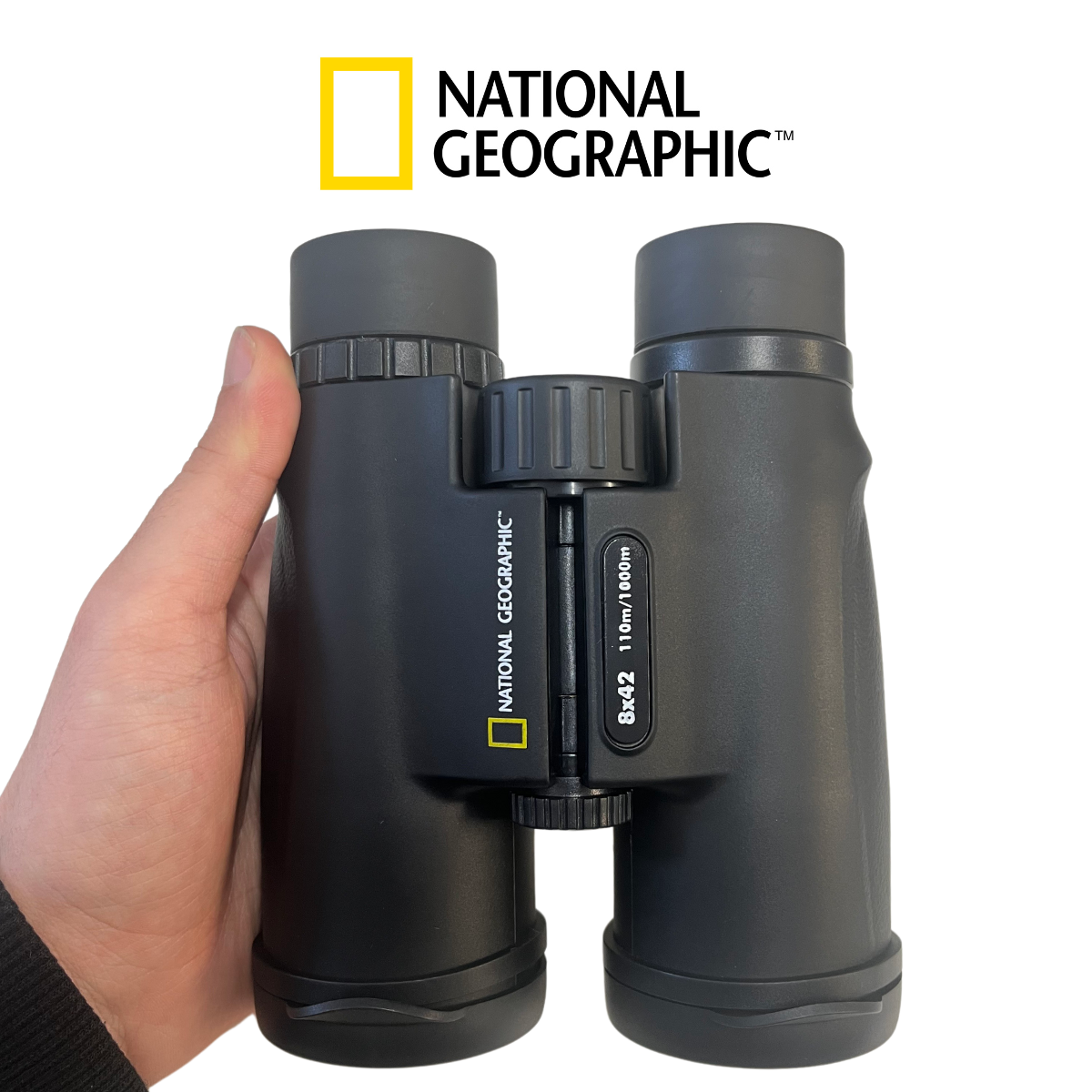 Mano sosteniendo binoculares negros, con logo National Geographic, sobre fondo blanco.