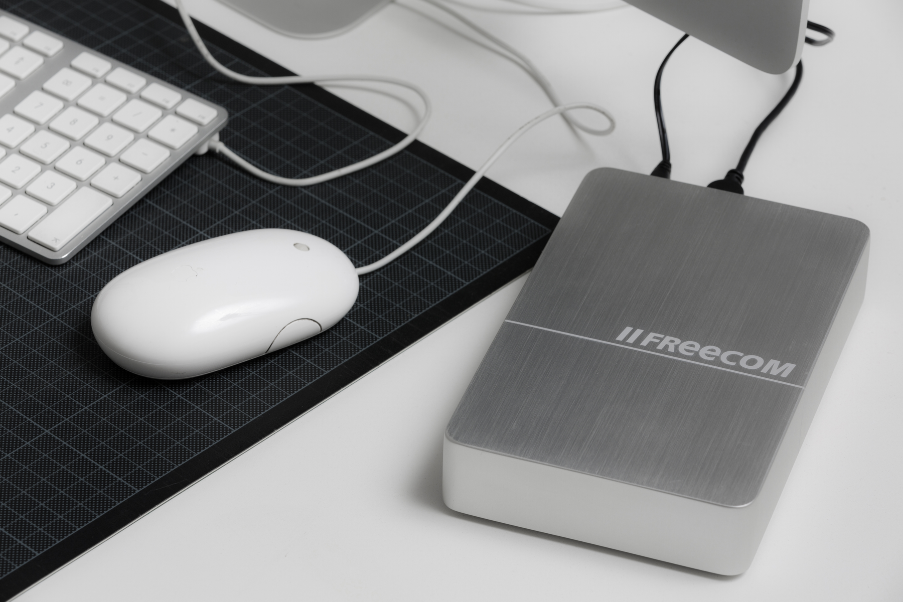 Zewnętrzny dysk twardy Freecom na biurku z białą myszą i klawiaturą. Podłączony do komputera.