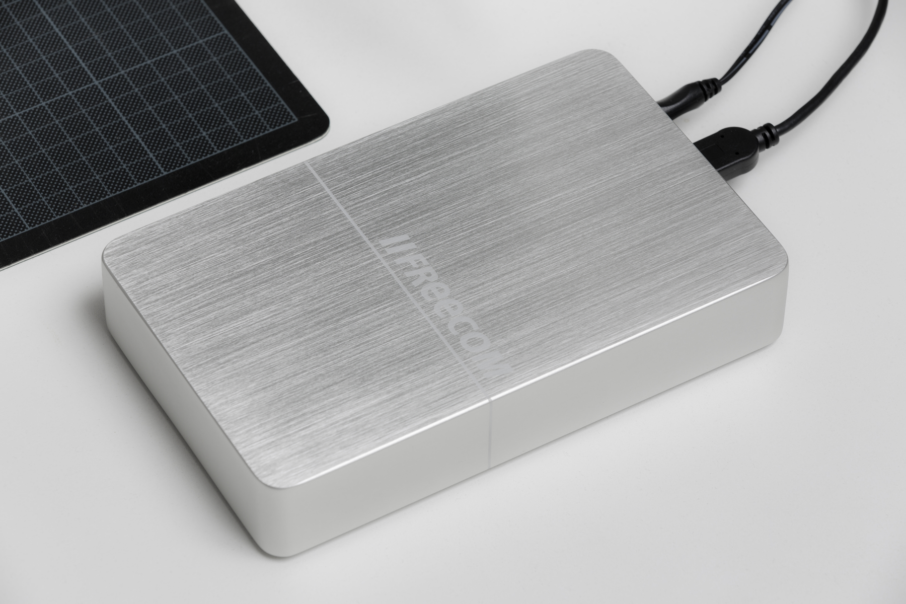 Zewnętrzny dysk twardy z panelem słonecznym obok. Białe tło. Widoczna marka Freecom.