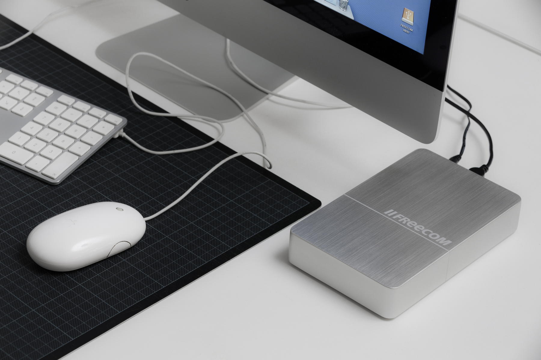 Konfiguracja komputera z monitorem, klawiaturą, myszą i srebrnym zewnętrznym dyskiem twardym.