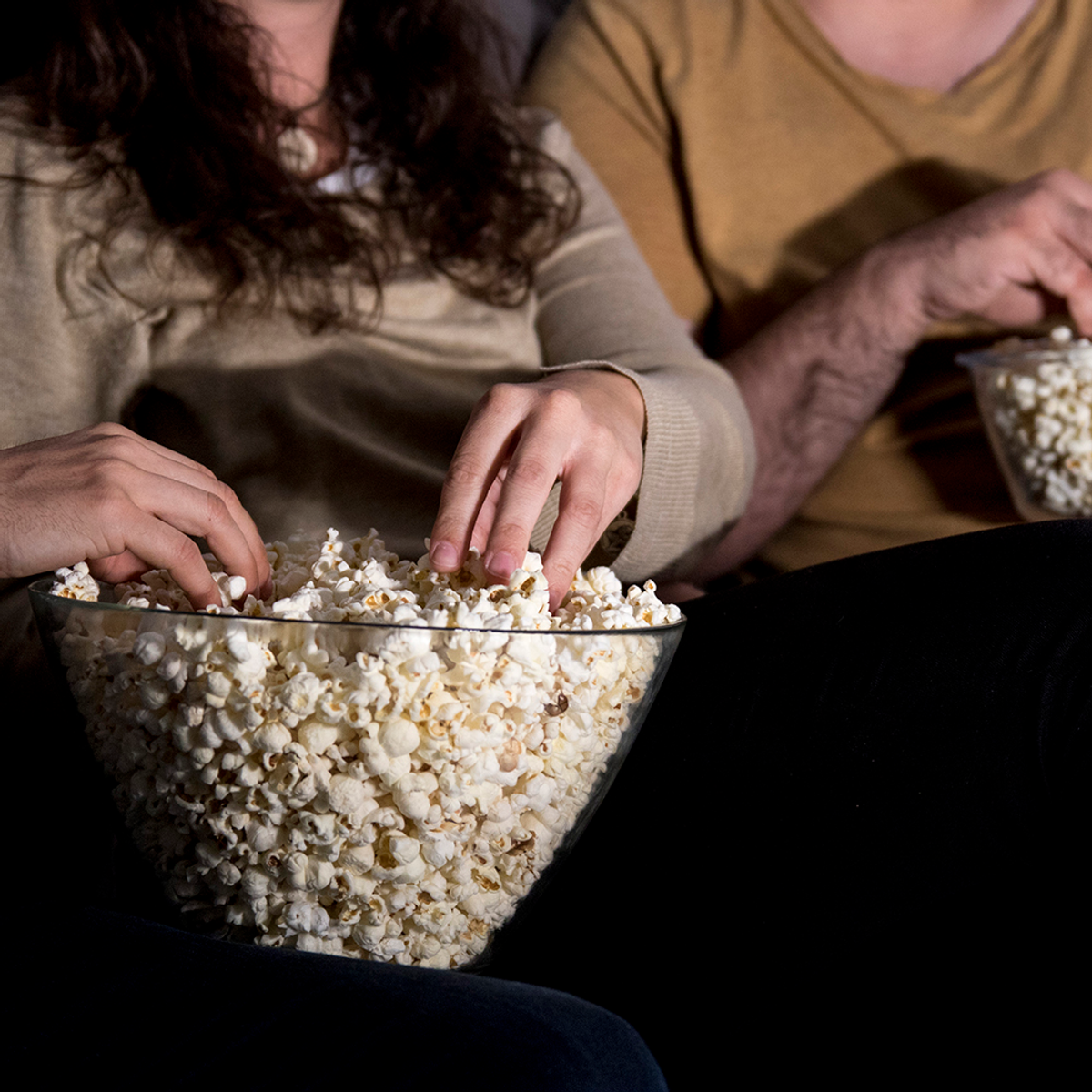 Una coppia è seduta e mangia popcorn da una grande ciotola di vetro.