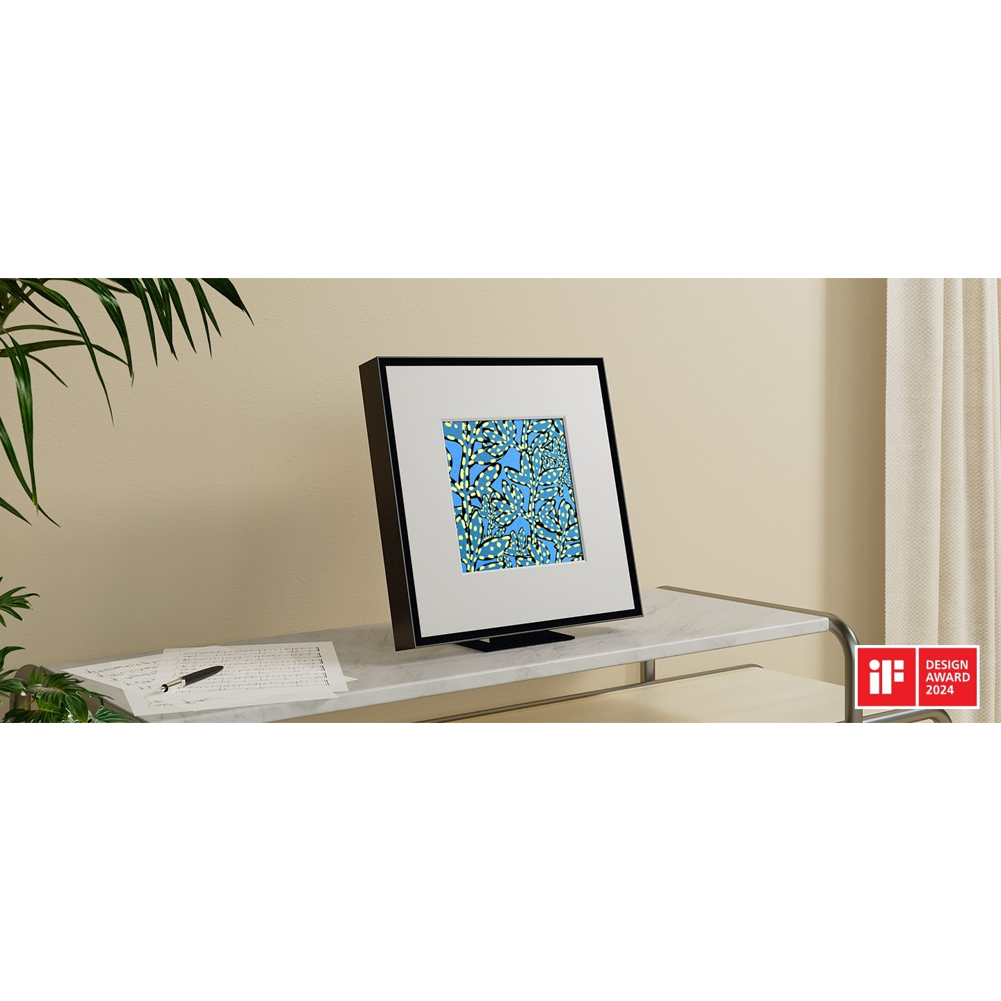 Oprawione dzieło sztuki na białej powierzchni. Po lewej roślina. Po prawej logo nagrody za design.
