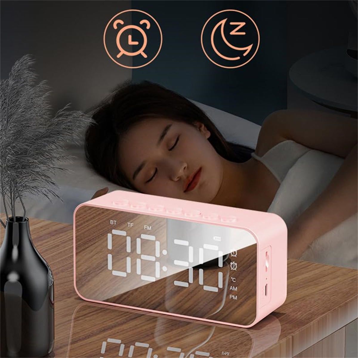 Rosa Wecker auf einem Holztisch. Im Hintergrund schläft eine Frau. Die Uhr zeigt die Zeit an.