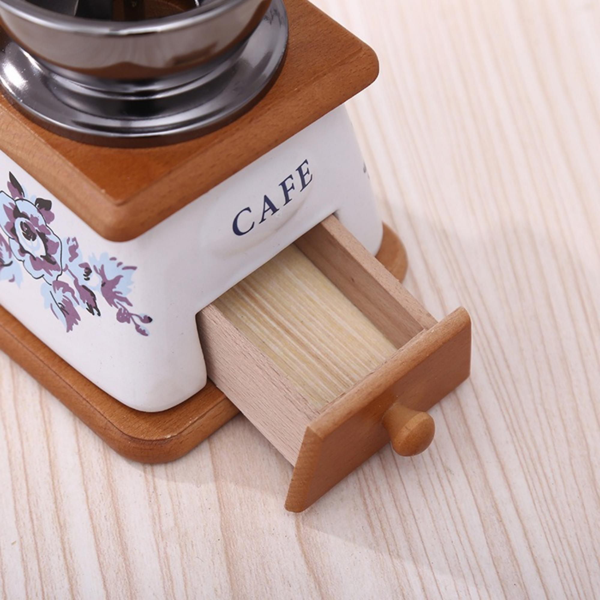 Eine hölzerne Kaffeemühle mit geöffneter Schublade. Die Mühle hat ein Blumendesign und 'CAFE' darauf geschrieben.