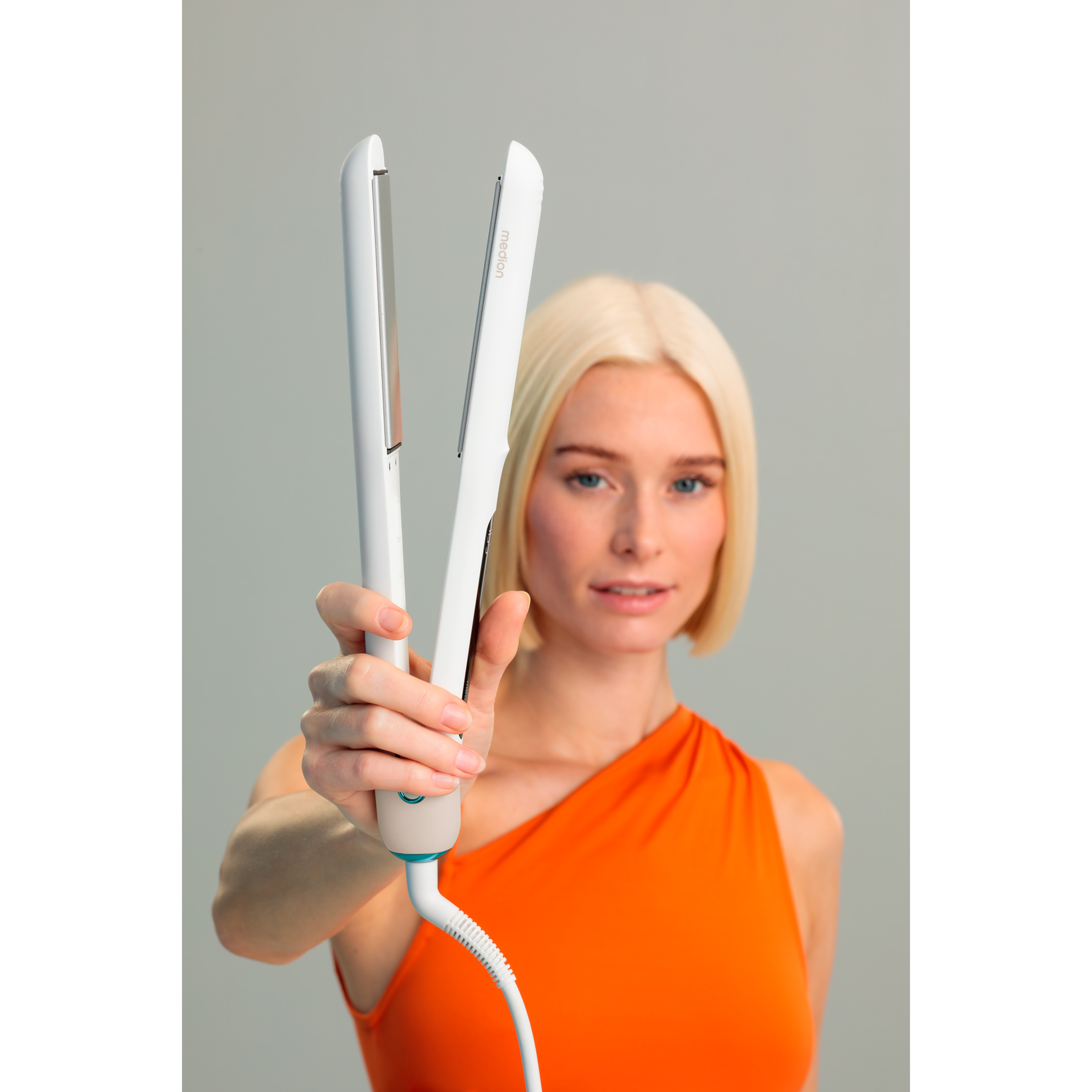 Kobieta trzymająca białą prostownicę przed sobą.