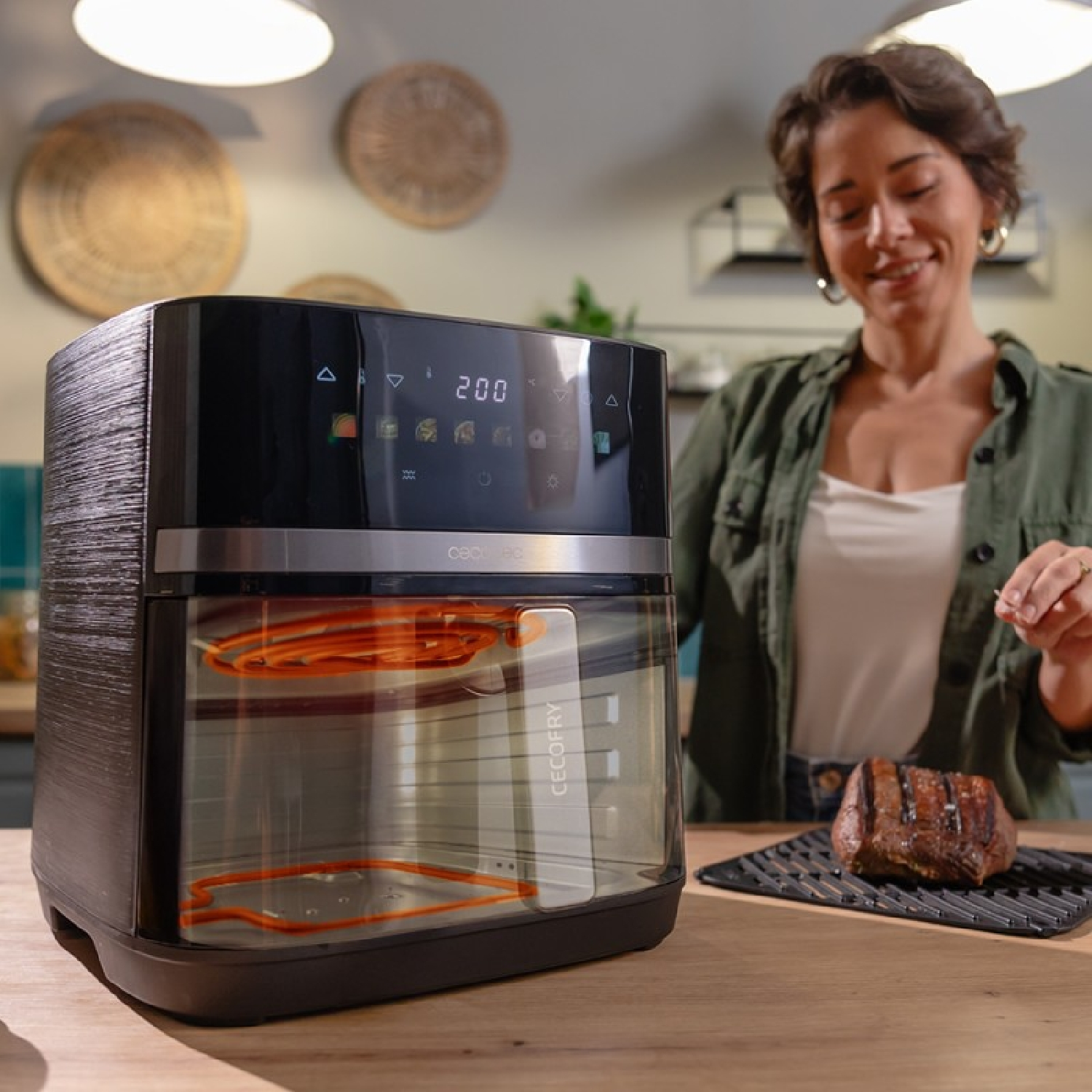 Kobieta uśmiecha się obok czarnej frytownicy powietrznej ze szklanymi drzwiami, obok upieczonego steku.