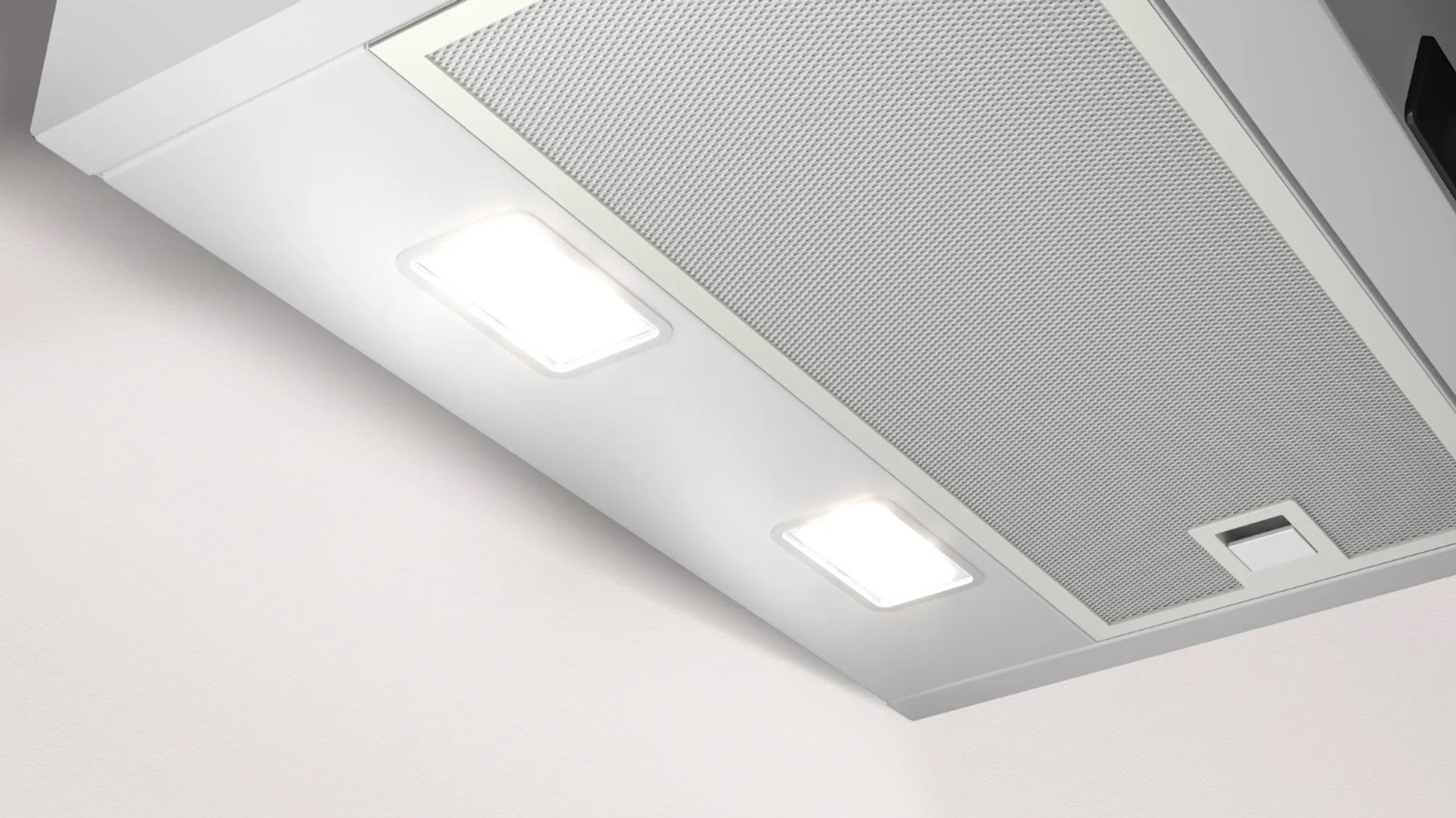 Primer plano de una campana extractora blanca con dos luces brillantes y un filtro de malla metálica.