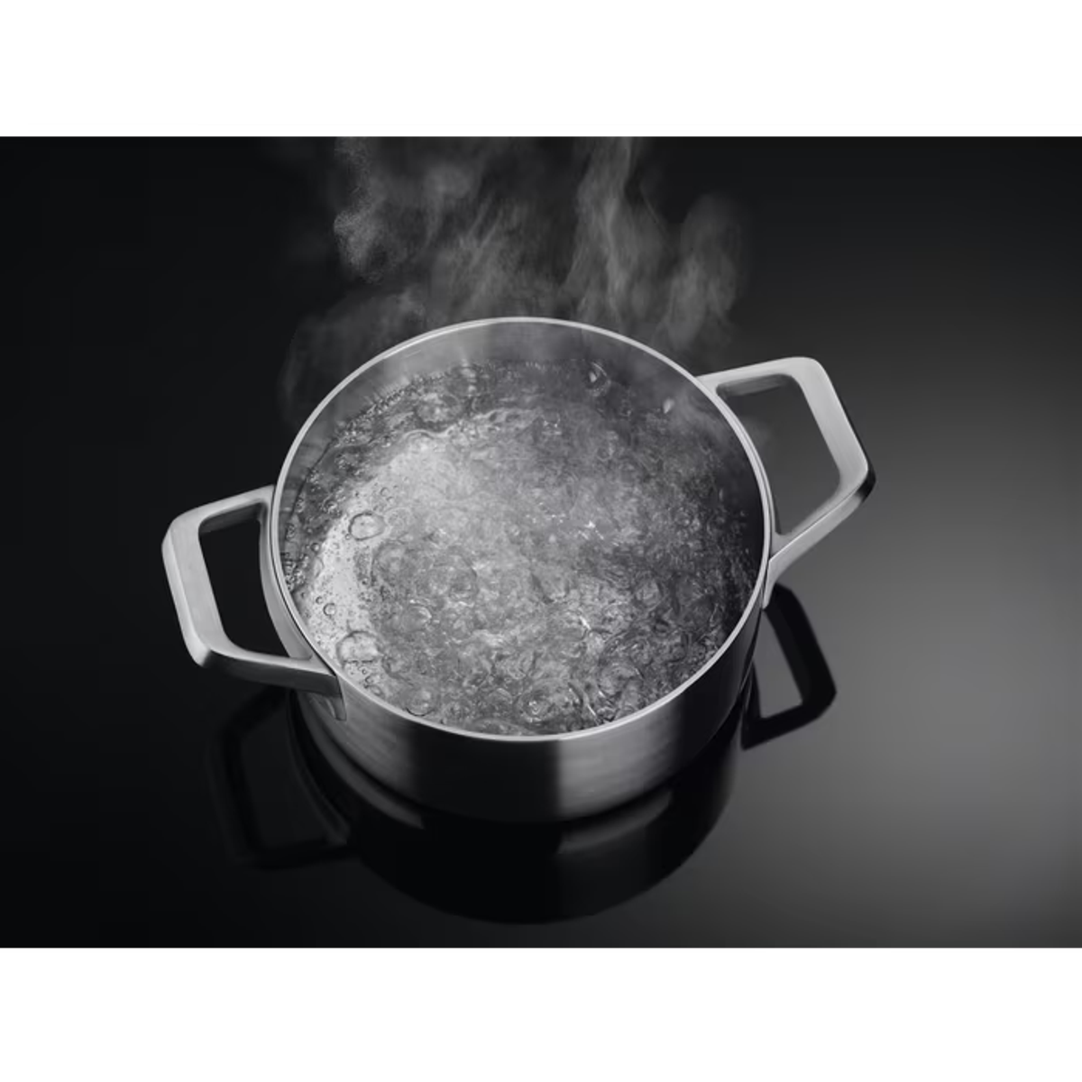 Una olla de acero inoxidable con agua hirviendo, vapor ascendente. Fondo negro.