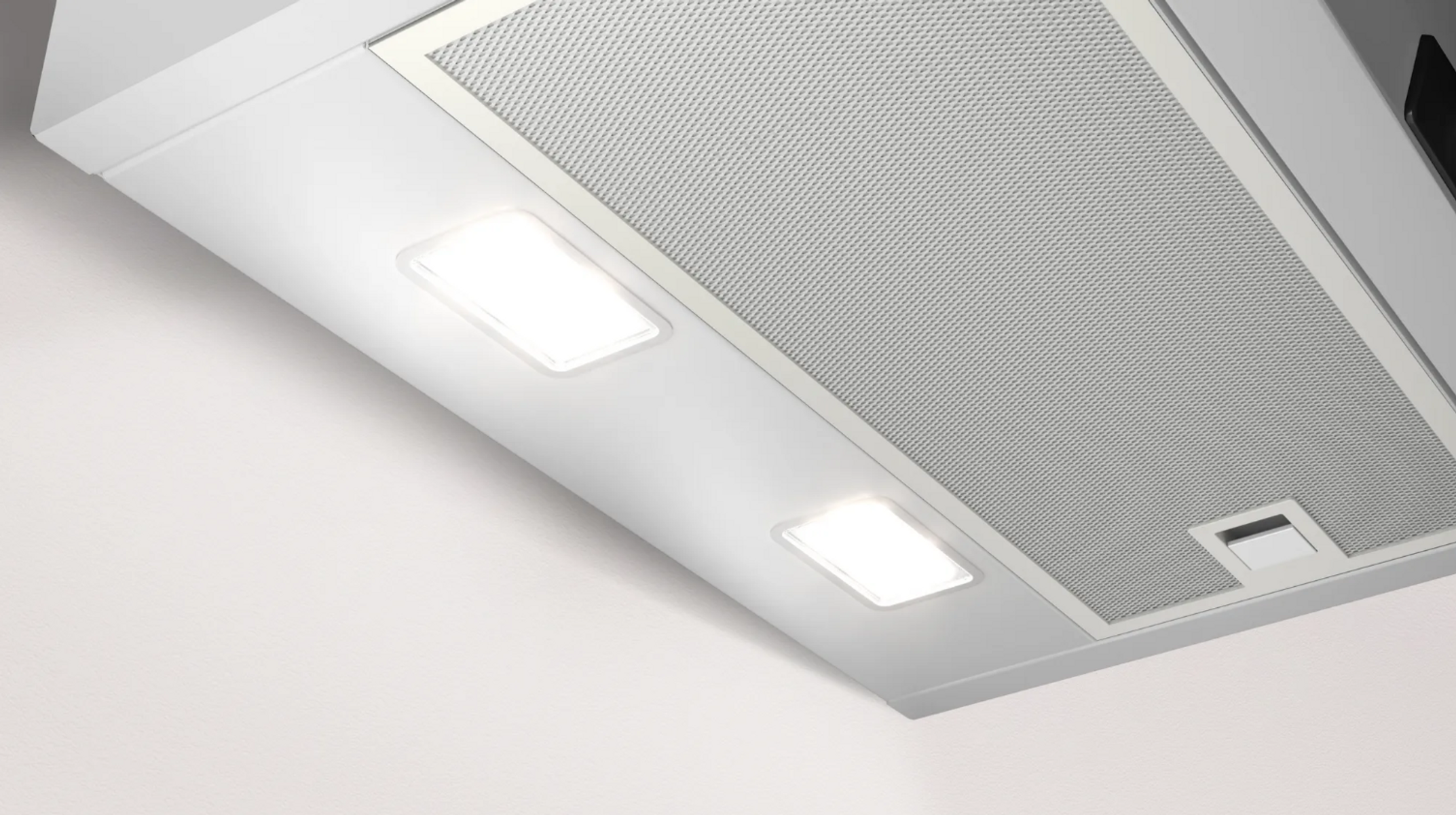 Una campana extractora blanca con dos luces brillantes, una malla metálica y un techo blanco plano.