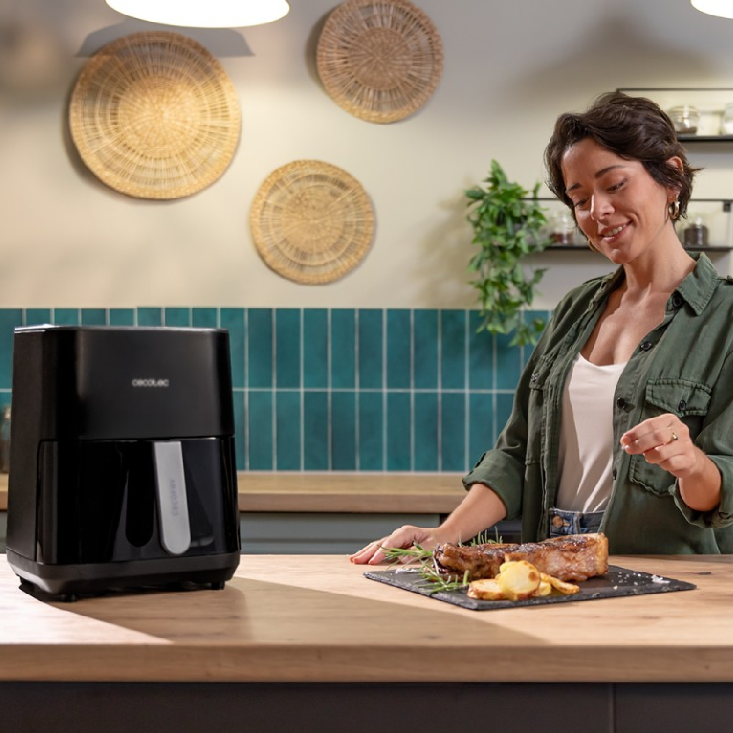 Kobieta z frytkownicą i jedzeniem na stole, w kuchni, z czarną frytkownicą.