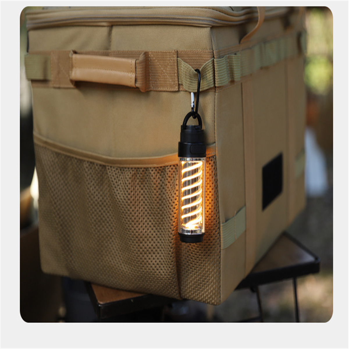Eine Campinglaterne, die an einer beigen Tasche hängt. Die Laterne leuchtet und hat ein Spirale.