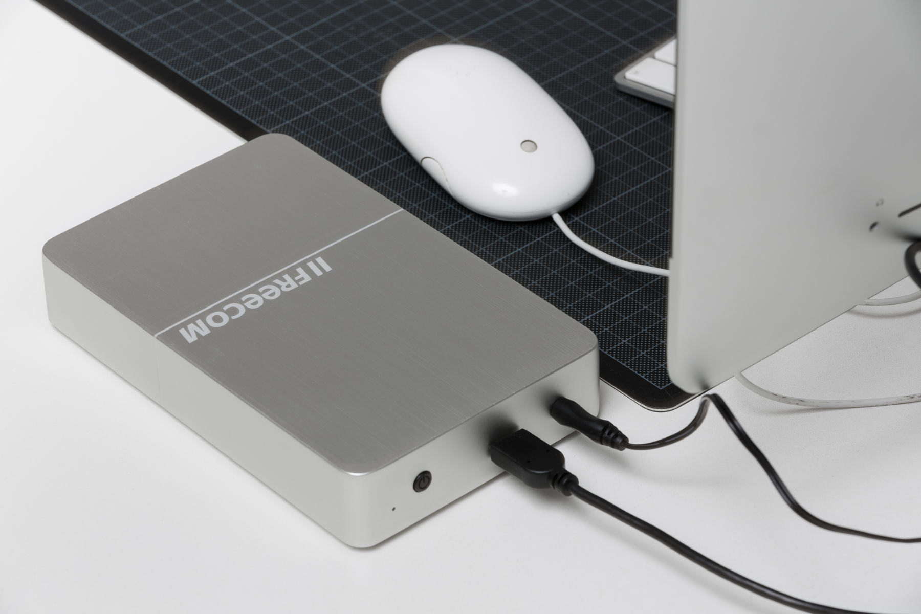 Srebrny zewnętrzny dysk twardy z czarnymi kablami i białą myszą na biurku.