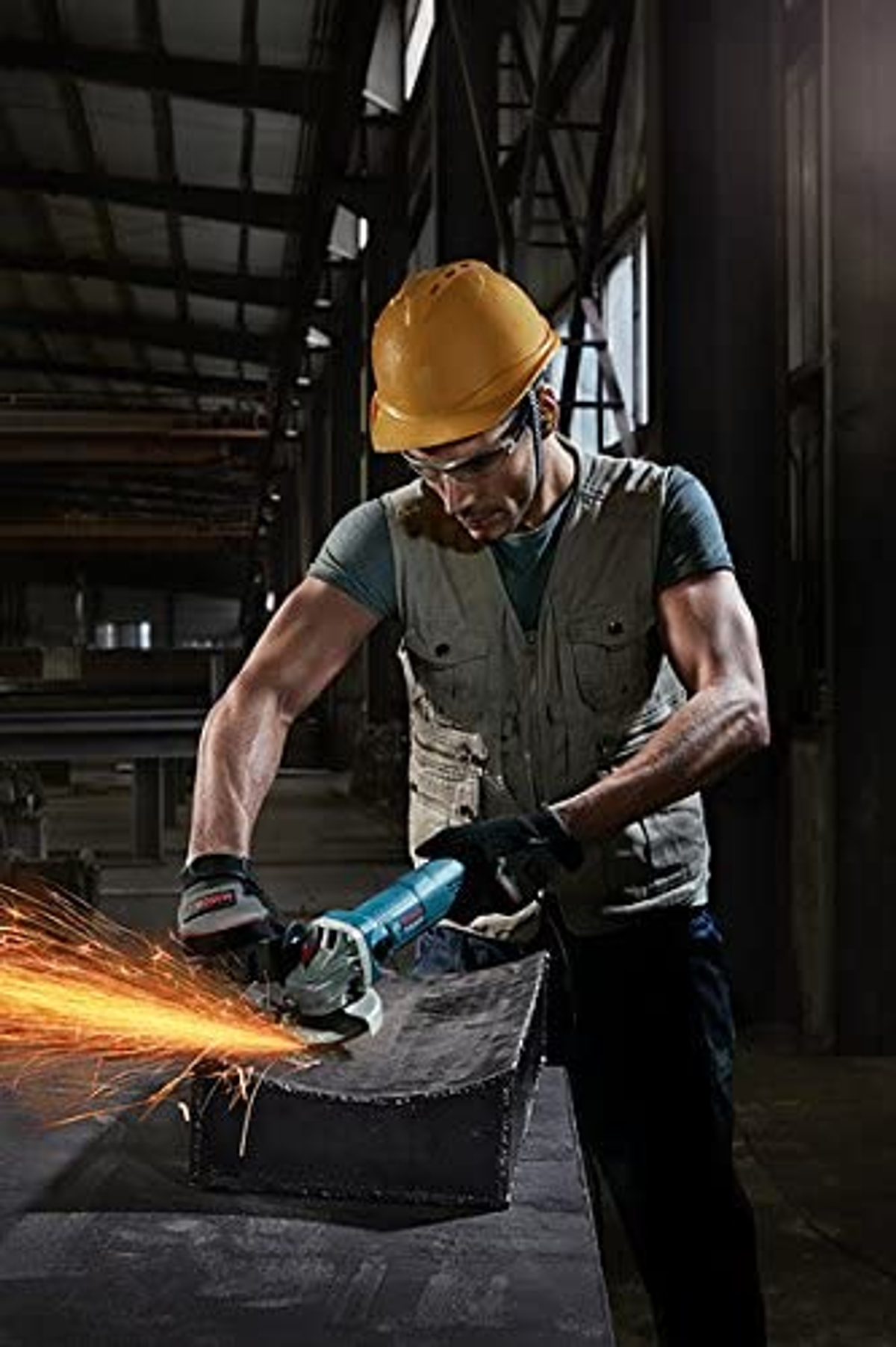 Mann mit gelbem Helm benutzt Winkelschleifer, Funken fliegen. Industrielle Umgebung.