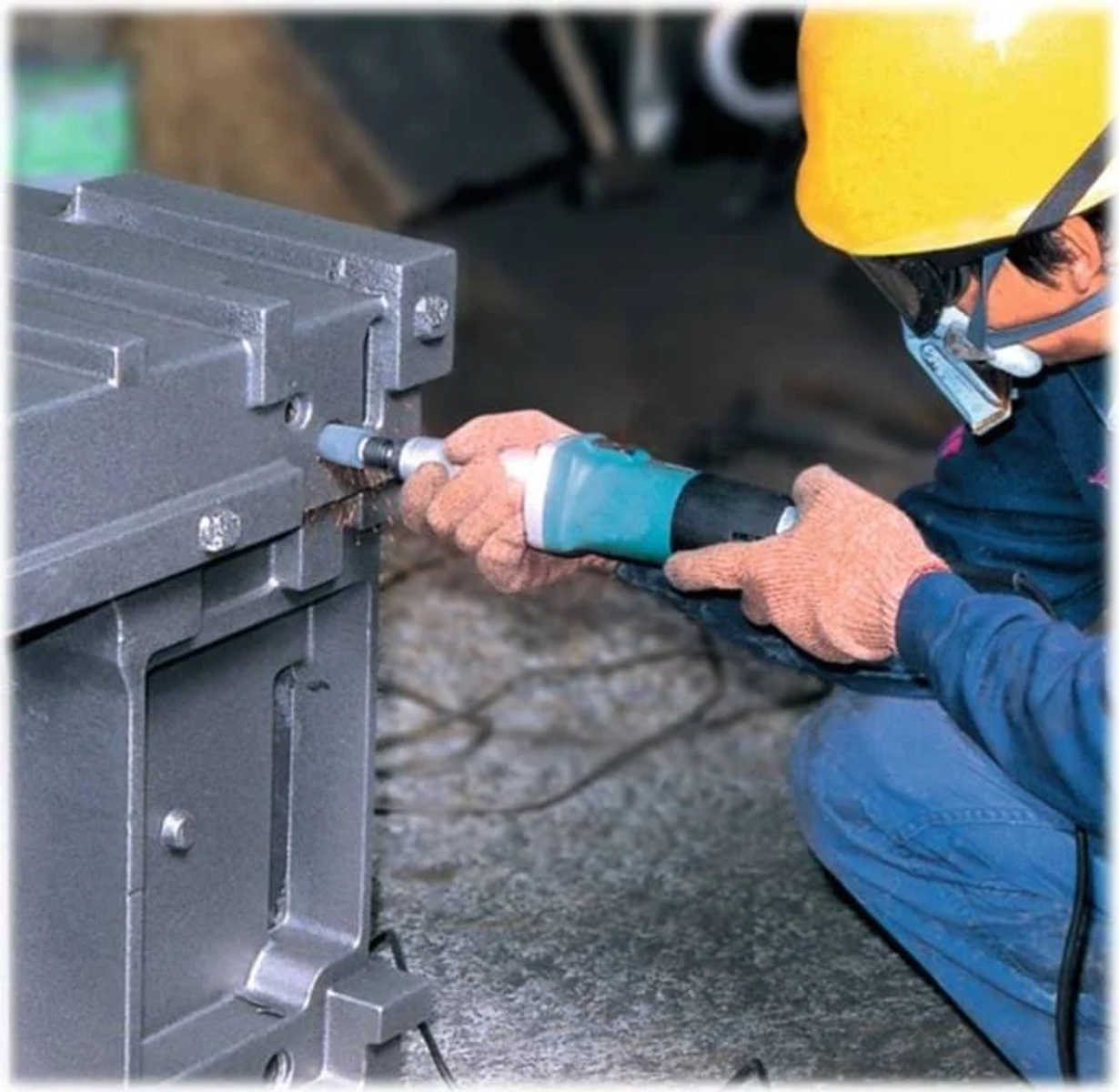 Osoba w żółtym kasku używa narzędzia na metalowym przedmiocie, tworząc iskry.