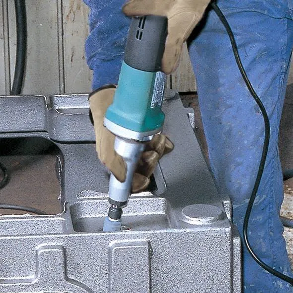 Osoba w dżinsach i rękawicach używająca szlifierki na metalowym przedmiocie.