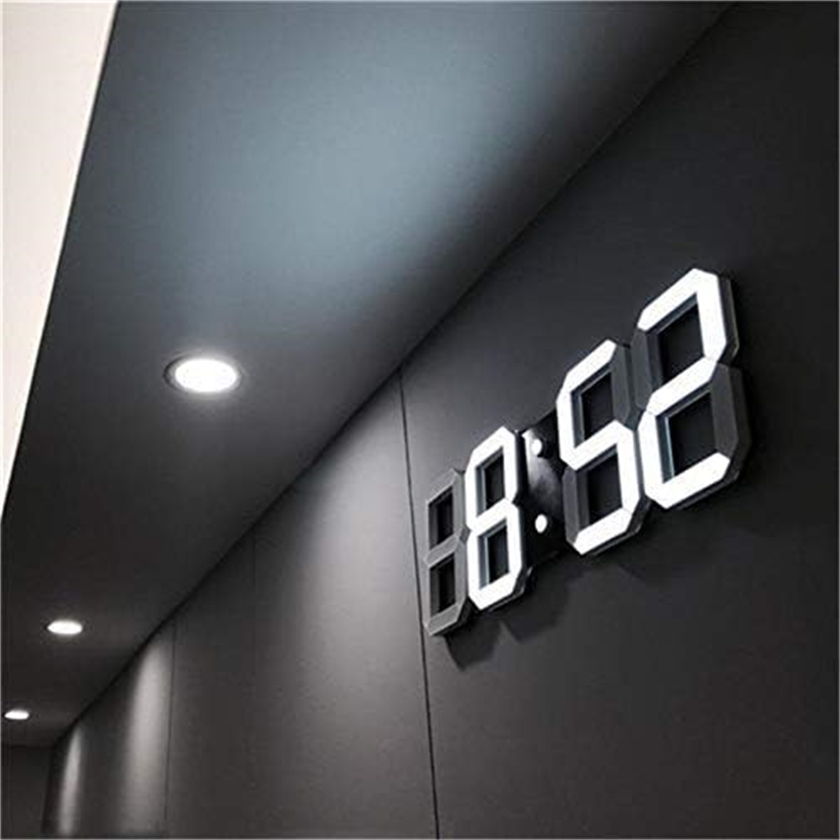 Digitaluhr an einer dunklen Wand, die 08:52 anzeigt. Die Wand hat drei Einbaustrahler.