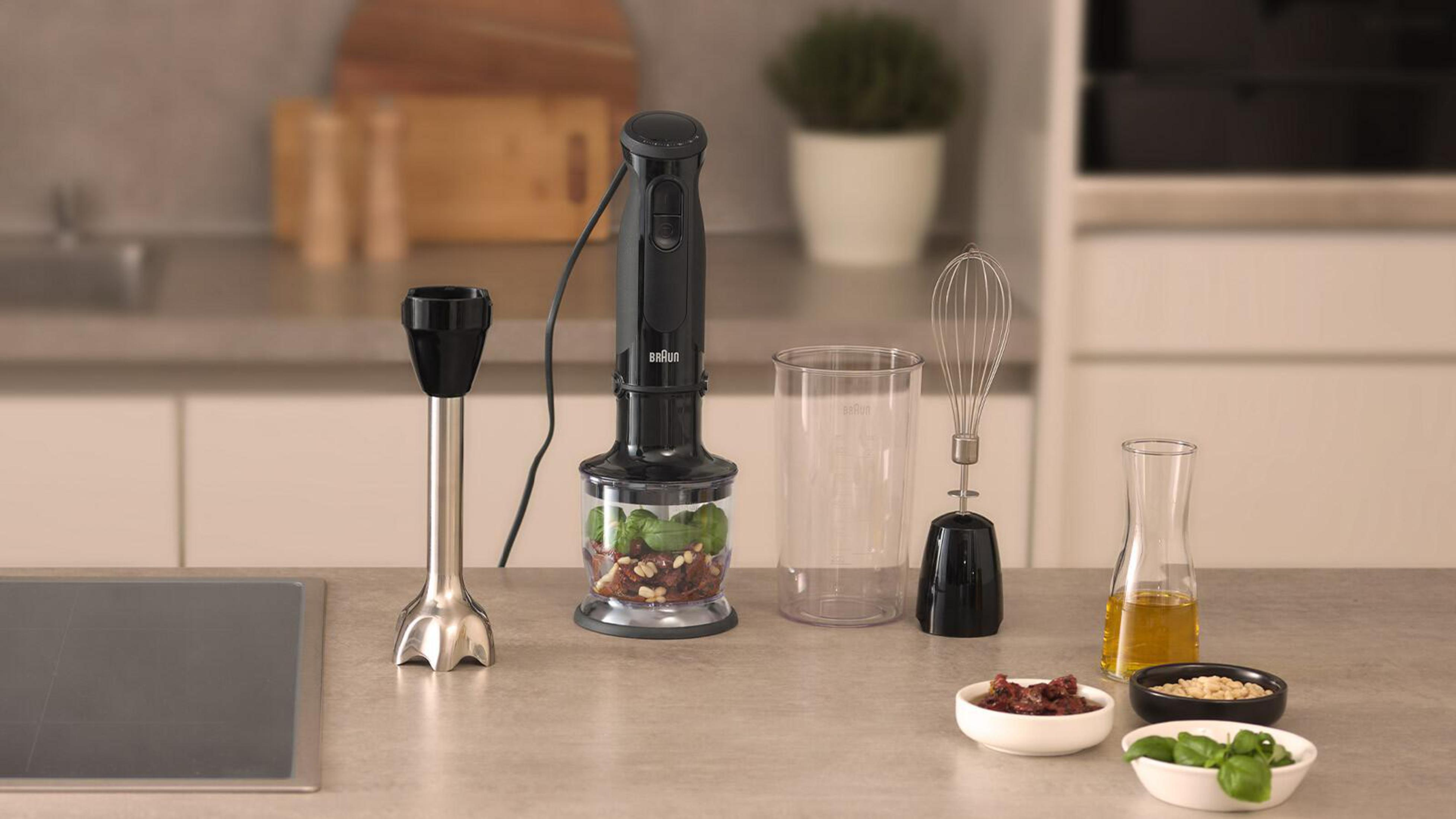 Frullatore a immersione nero e accessori disposti su un piano cucina.