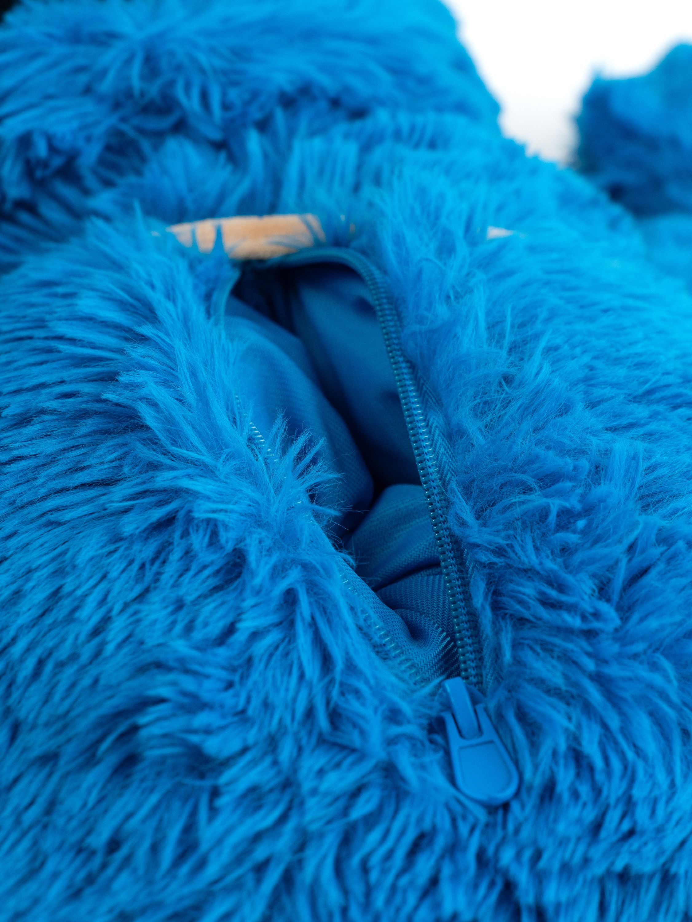 Nahaufnahme eines blauen, pelzigen Monsterkostüms mit teilweise offenem Reißverschluss.