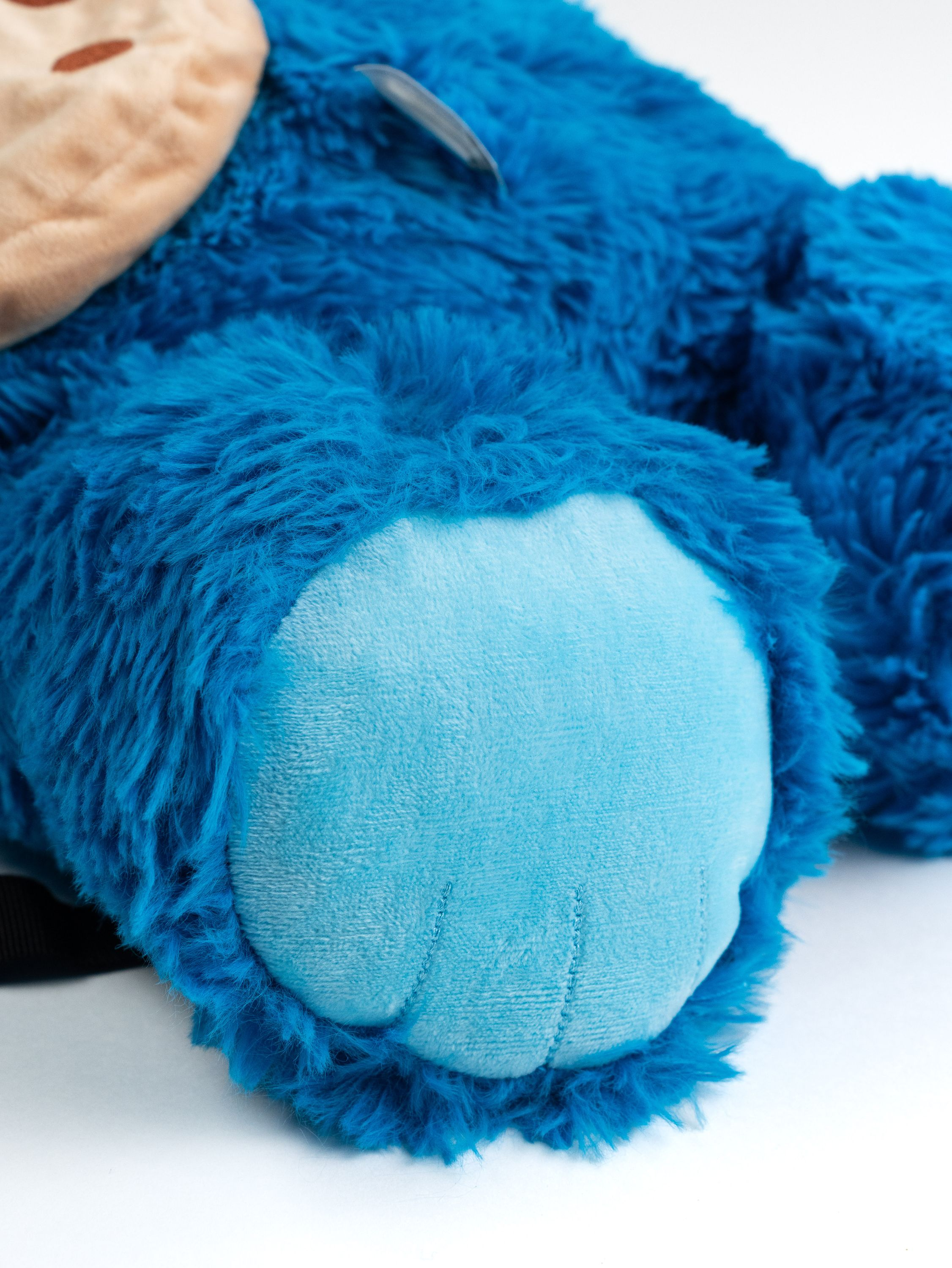 Nahaufnahme des Fußes eines Krümelmonster-Plüschtiers, blaue Haare und hellblaues Fußpolster auf weißem Grund.