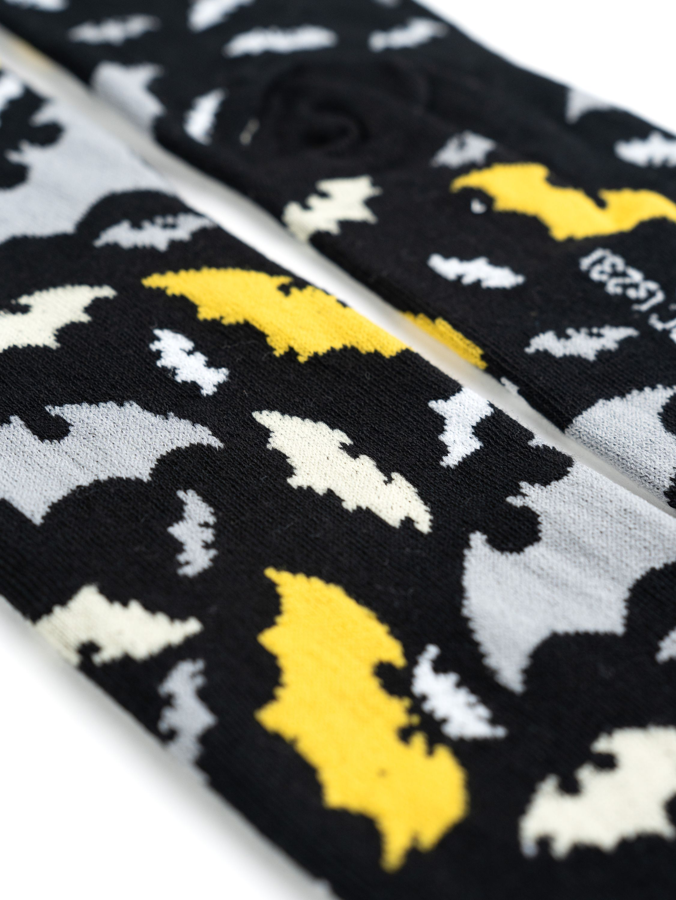 Zwei Socken mit Fledermausmustern, grau und gelb auf schwarzem Hintergrund.