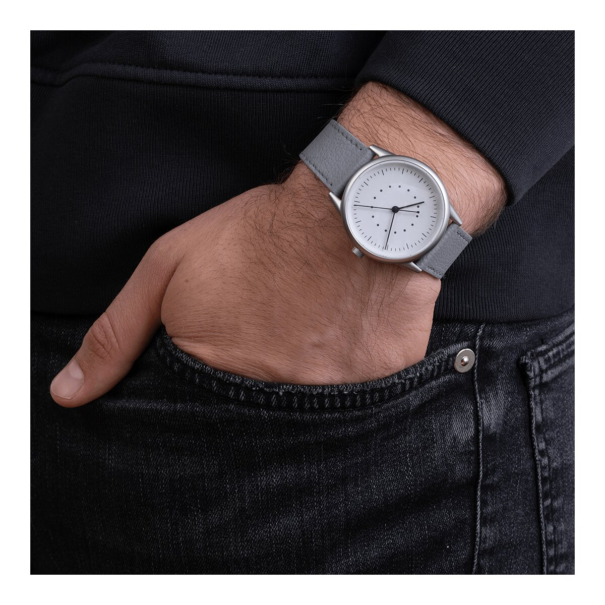 Das Handgelenk eines Mannes mit einer Uhr und einem grauen Armband, schwarze Jeans.
