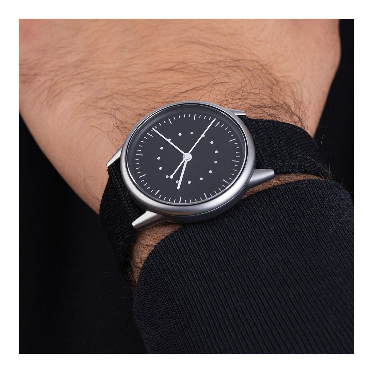 Mannes Handgelenk mit schwarzer Uhr. Die Uhr hat ein schwarzes Zifferblatt mit weißen Punkten und schwarzem Band.