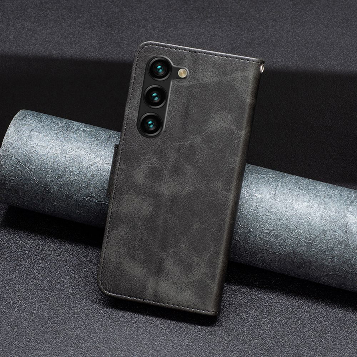Een grijze leren telefoonhoes met drie camera's. Het staat op een getextureerde grijze achtergrond.