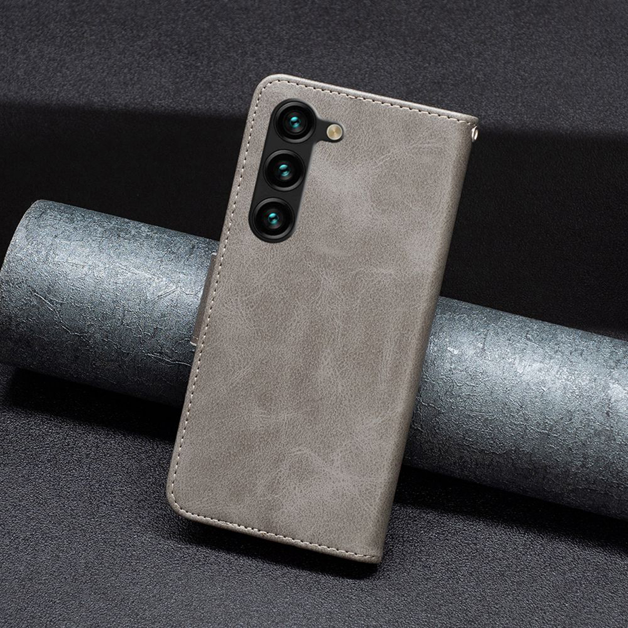 Een grijze leren telefoonhoes met drie camera's. Het staat op een getextureerde grijze achtergrond.