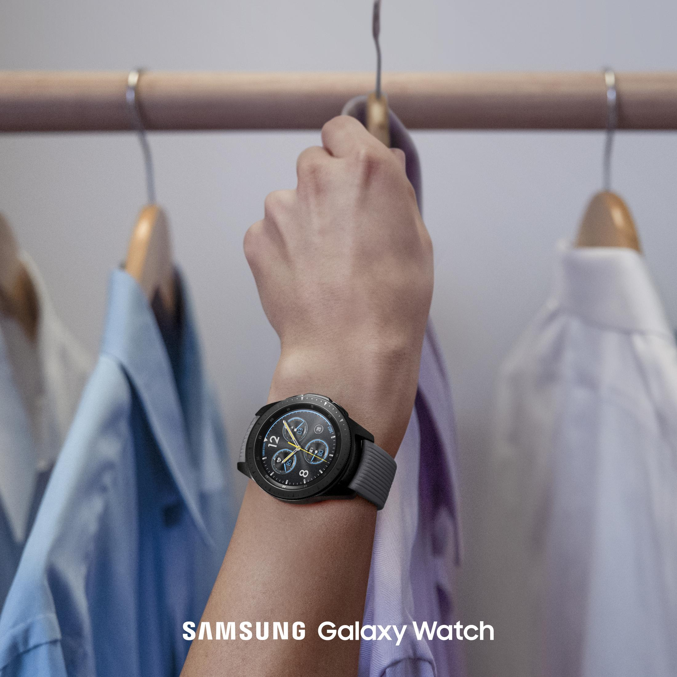Eine Person, die eine schwarze Smartwatch am Handgelenk trägt, vor Kleidung.