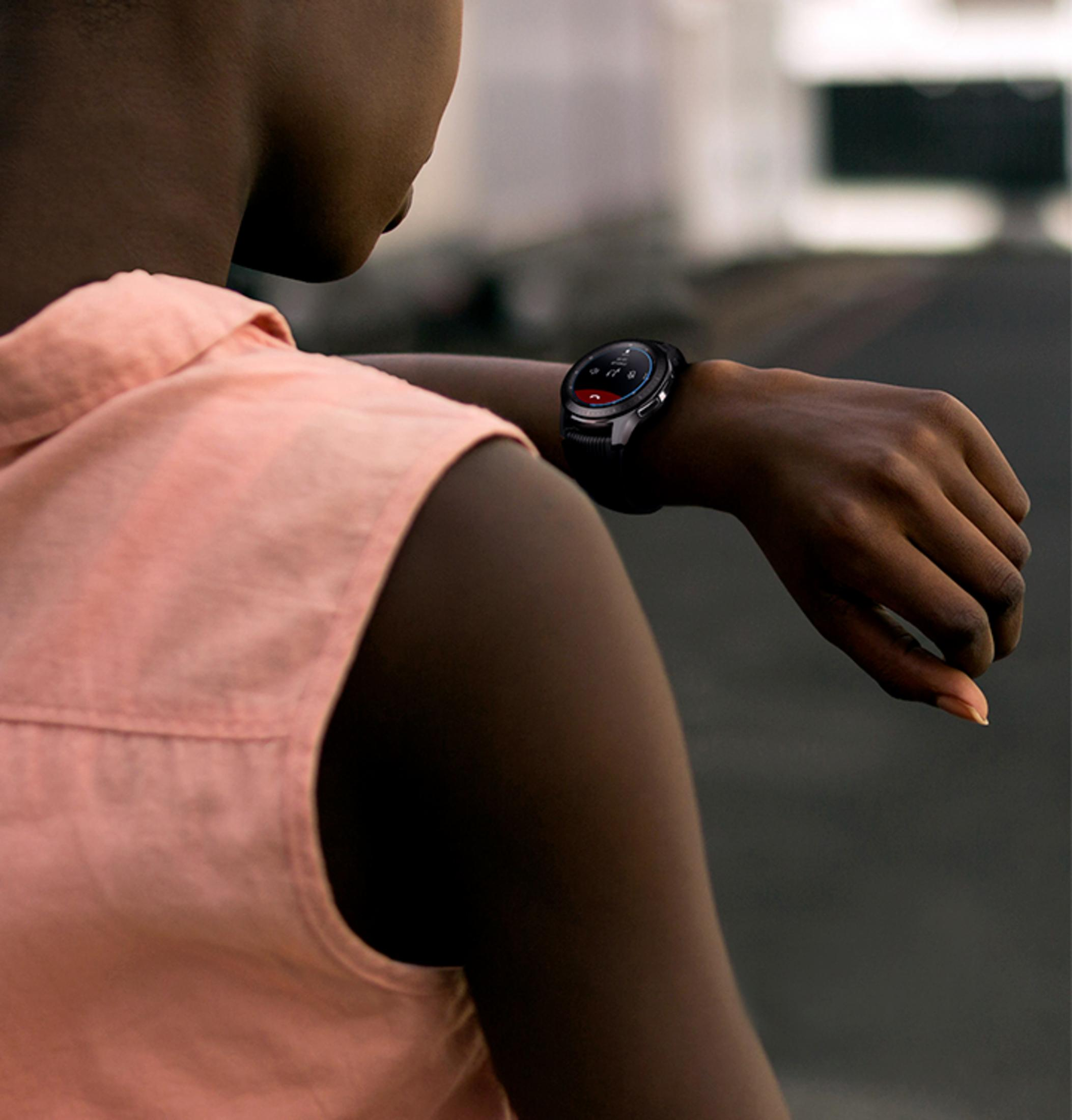 Eine Person mit rosa Hemd betrachtet eine Smartwatch am Handgelenk. Die Uhr ist schwarz und silber.