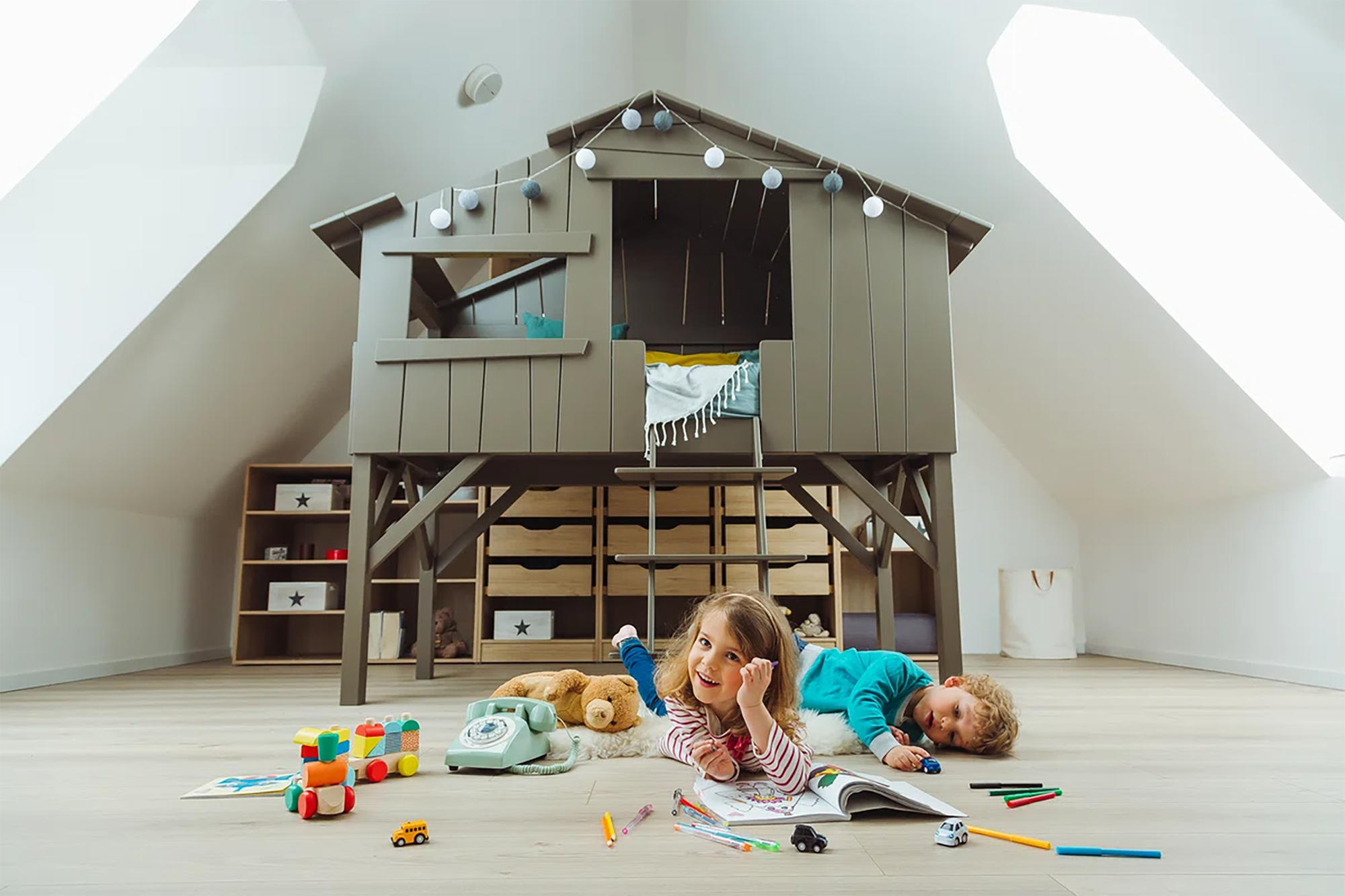 Twee kinderen in een speelkamer met een boomhut. Meisje lacht, jongen slaapt. Speelgoed en meubels.