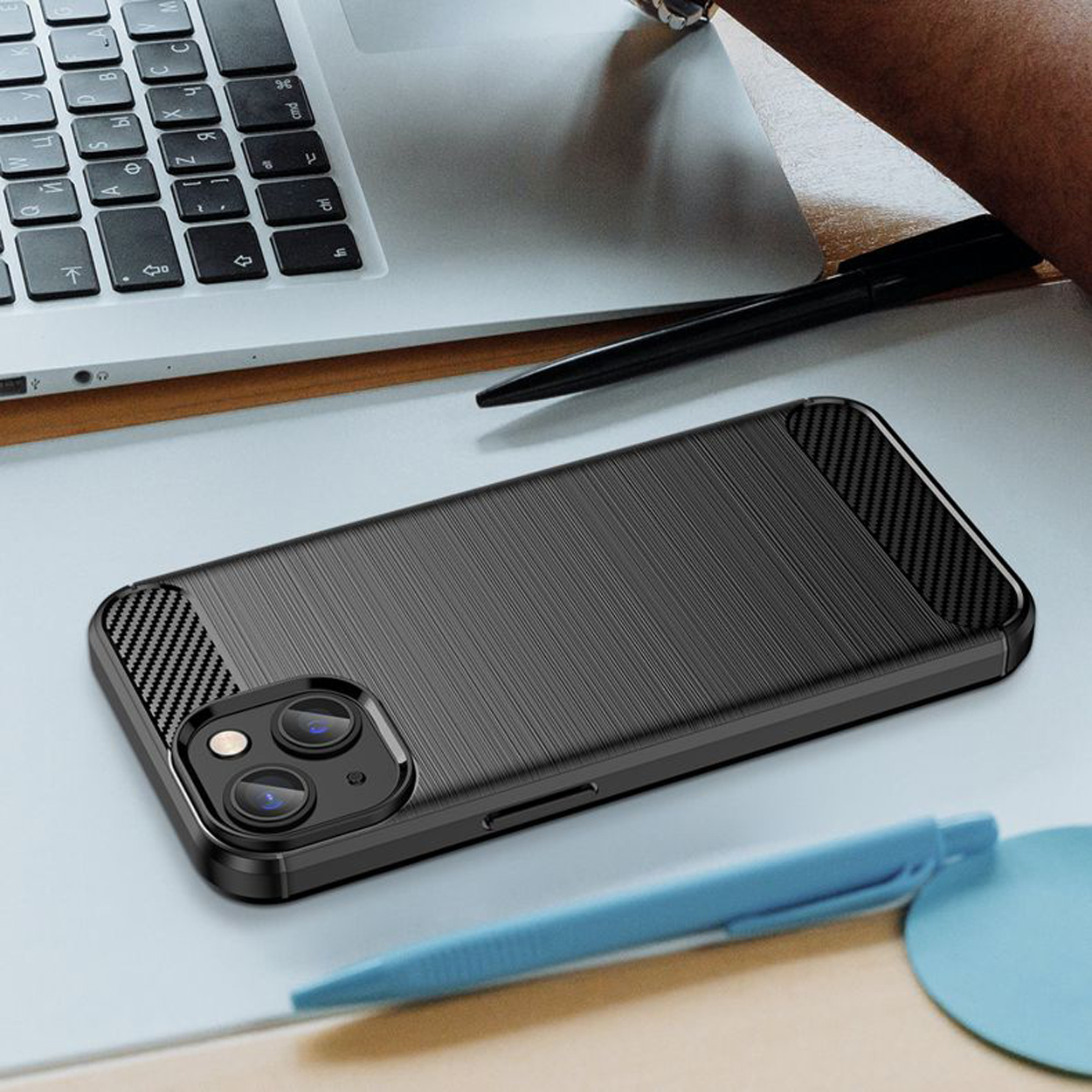 Coque de téléphone noire sur un bureau avec un ordinateur portable et un stylo. Elle a une texture fibre de carbone.