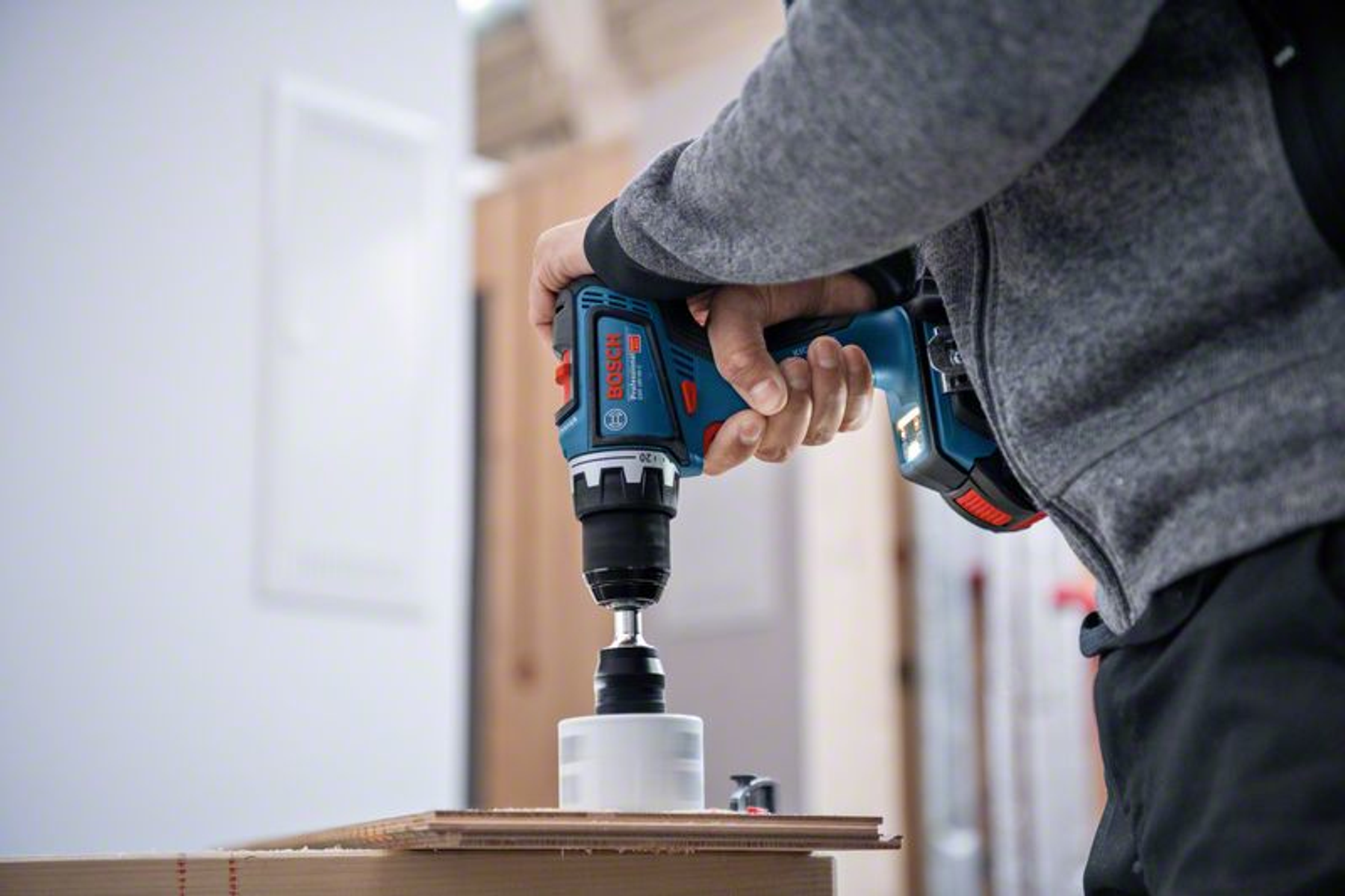 Una persona perforando un agujero en una tabla de madera con un taladro eléctrico azul y negro.