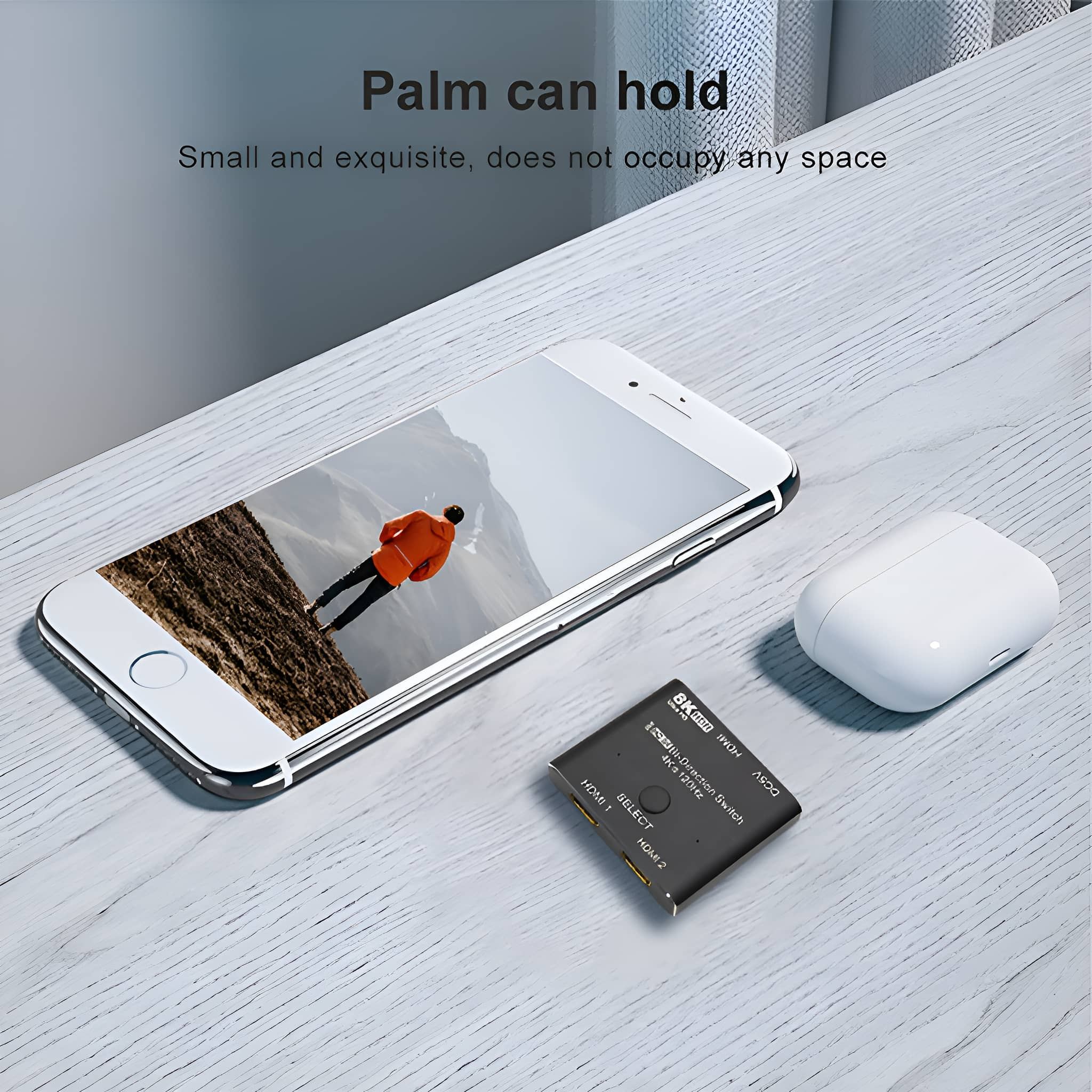 Ein Telefon, kabellose Ohrhörer und ein schwarzer HDMI-Switch auf einer Holzoberfläche.