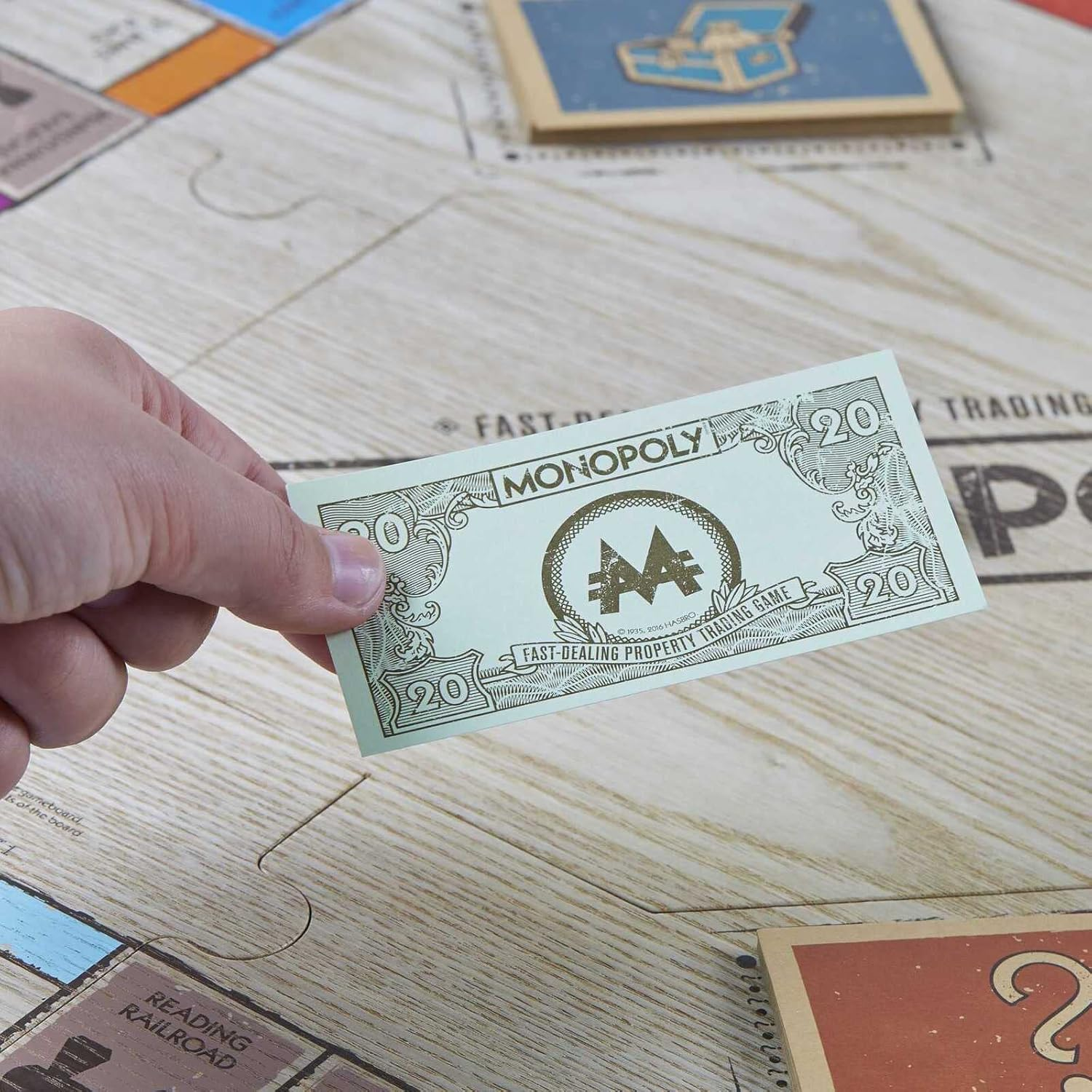 Hand hält eine Monopoly 20-Dollar-Note auf einem Monopoly-Spielbrett mit anderen Spielkarten.