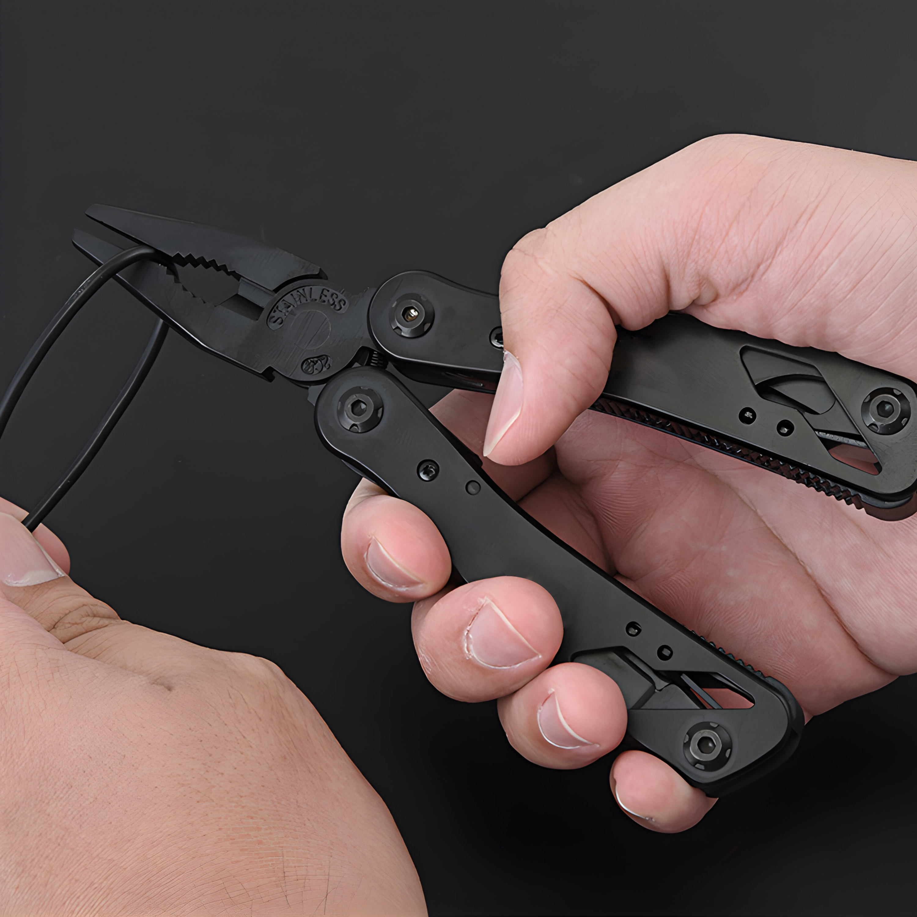 Schwarze Multitool-Zange in Händen, die einen schwarzen Draht vor schwarzem Hintergrund schneidet.