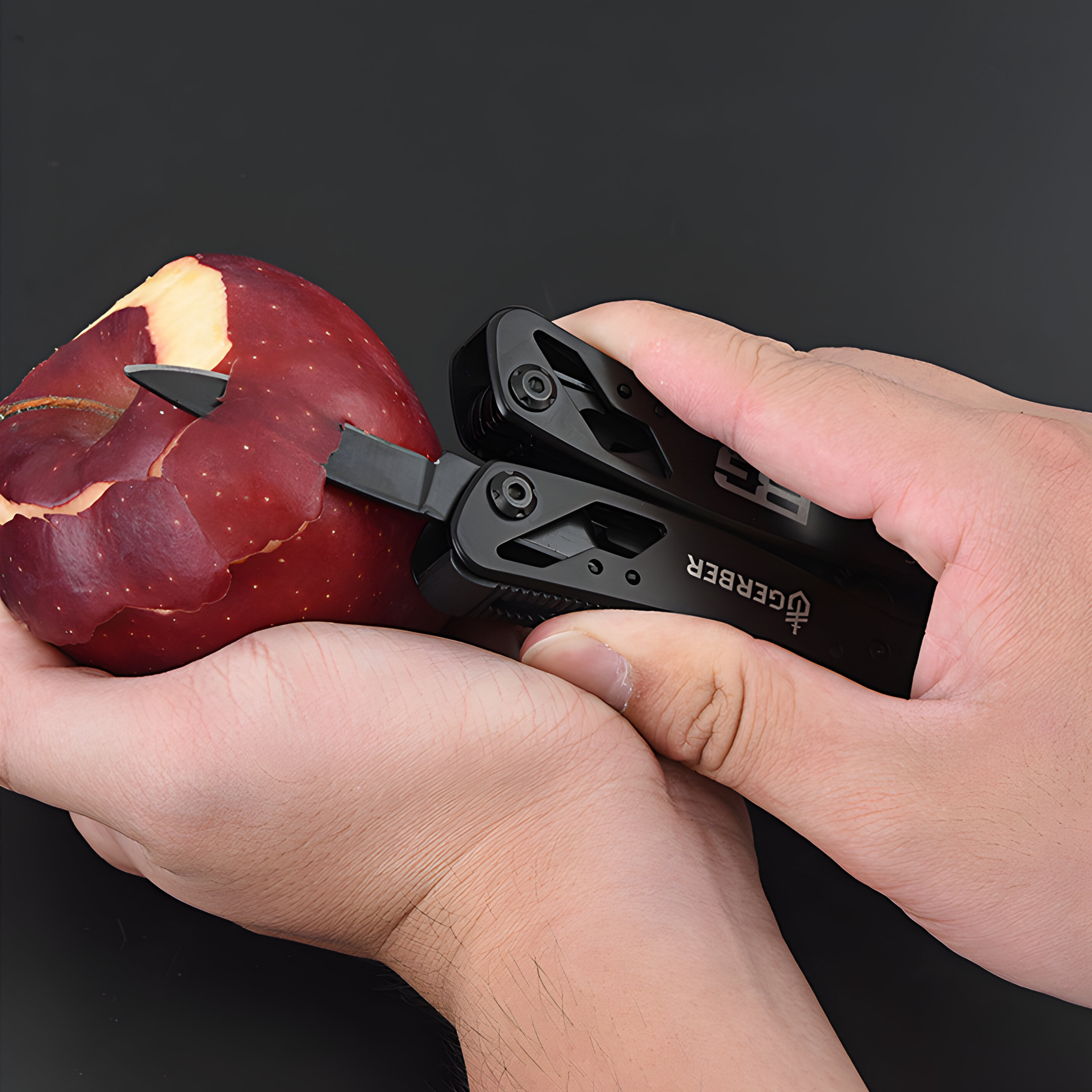 Hände halten ein schwarzes Multitool, das einen Apfel schneidet. Roter Apfel mit geschältem Bereich.