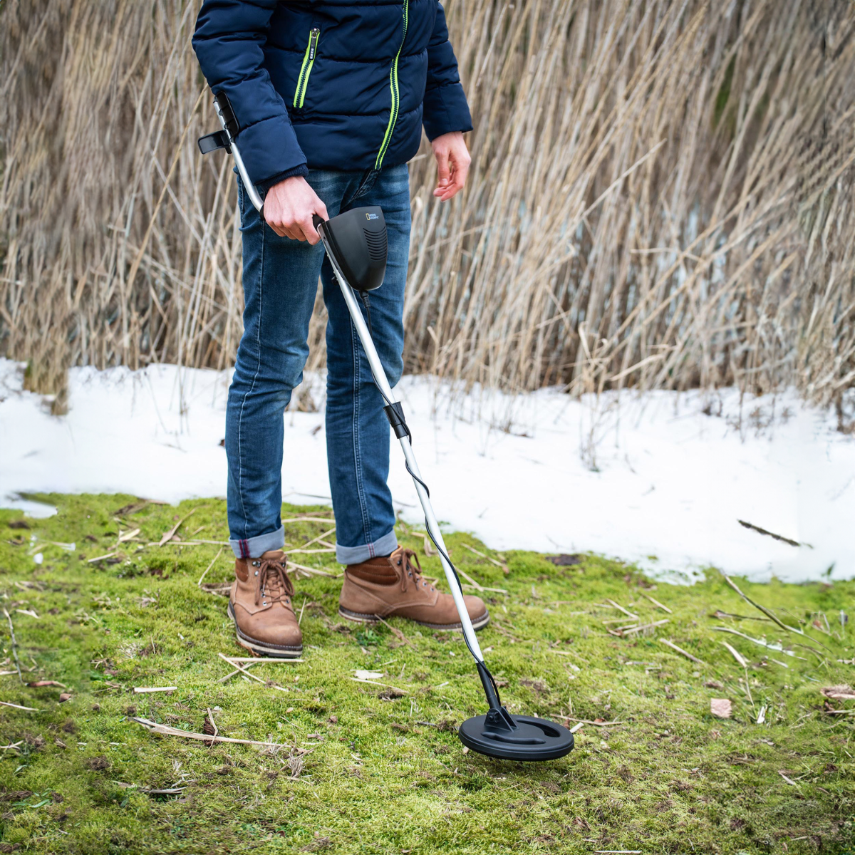 Persona usando detector de metales en campo con hierba y nieve.