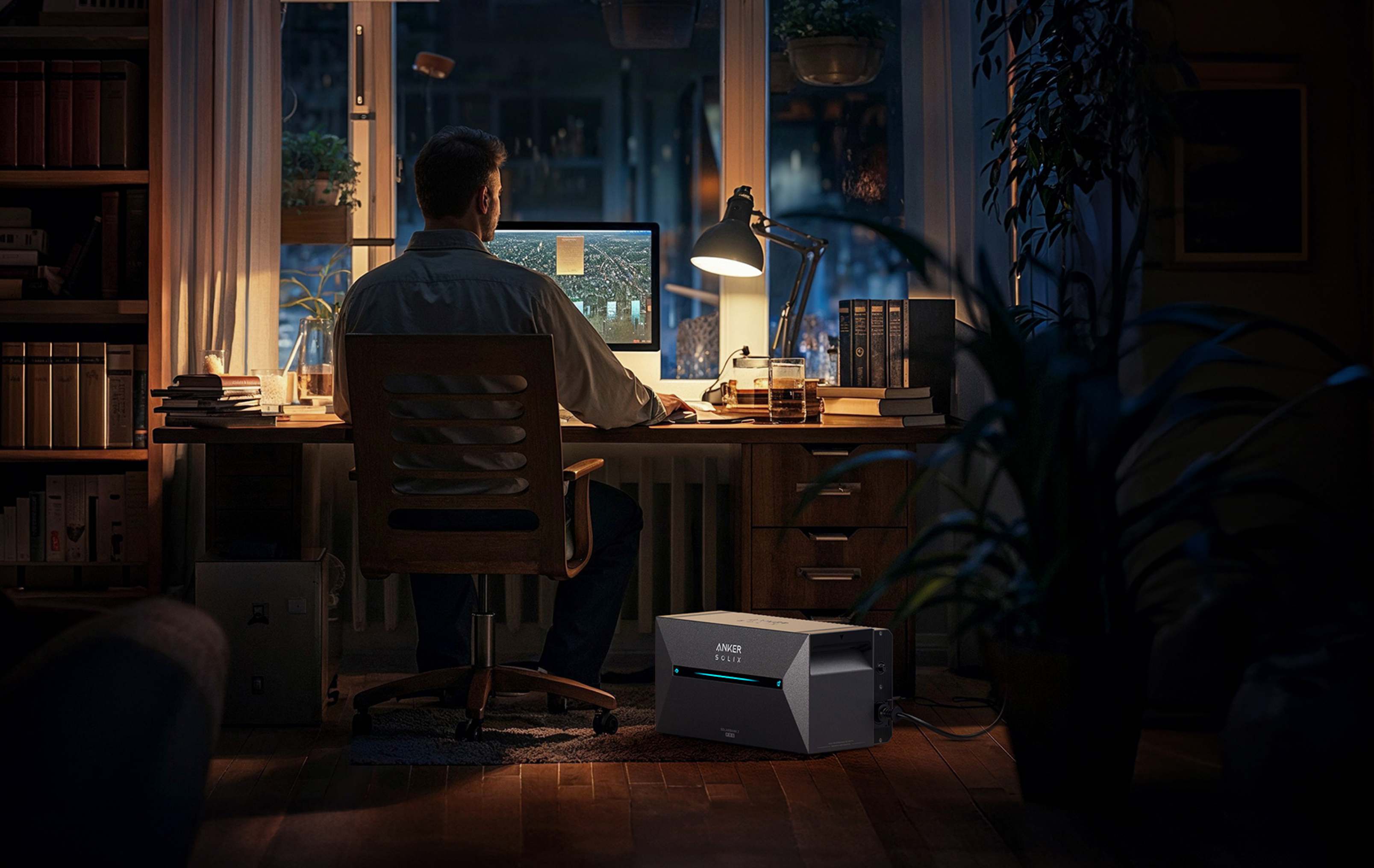 Mężczyzna pracuje przy biurku z komputerem, w słabo oświetlonym pokoju.