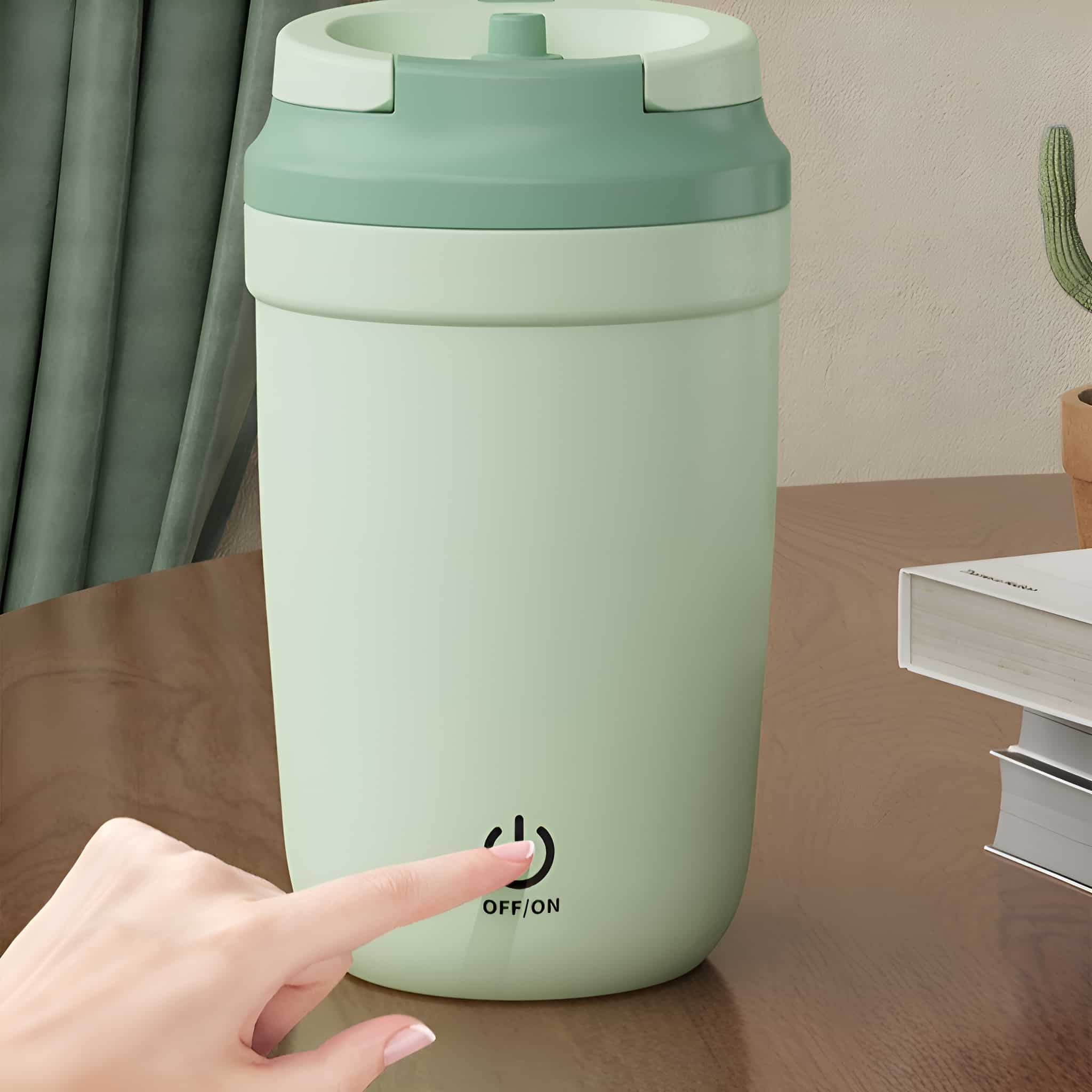 Ein kleiner, mintgrüner elektrischer Reisebecher mit einer Hand, die den Einschaltknopf drückt.