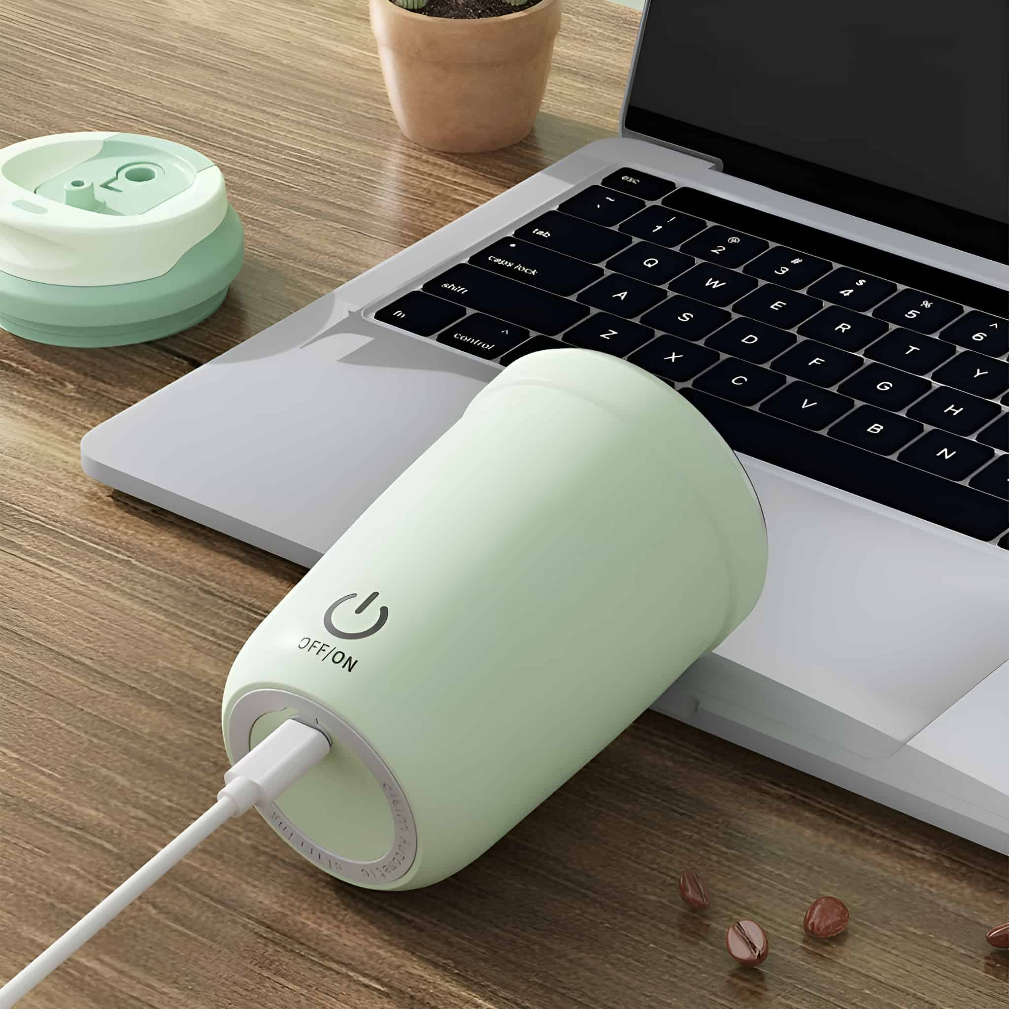 Ein hellgrüner Reisebecher mit Ladekabel, das an einen Laptop angeschlossen ist.